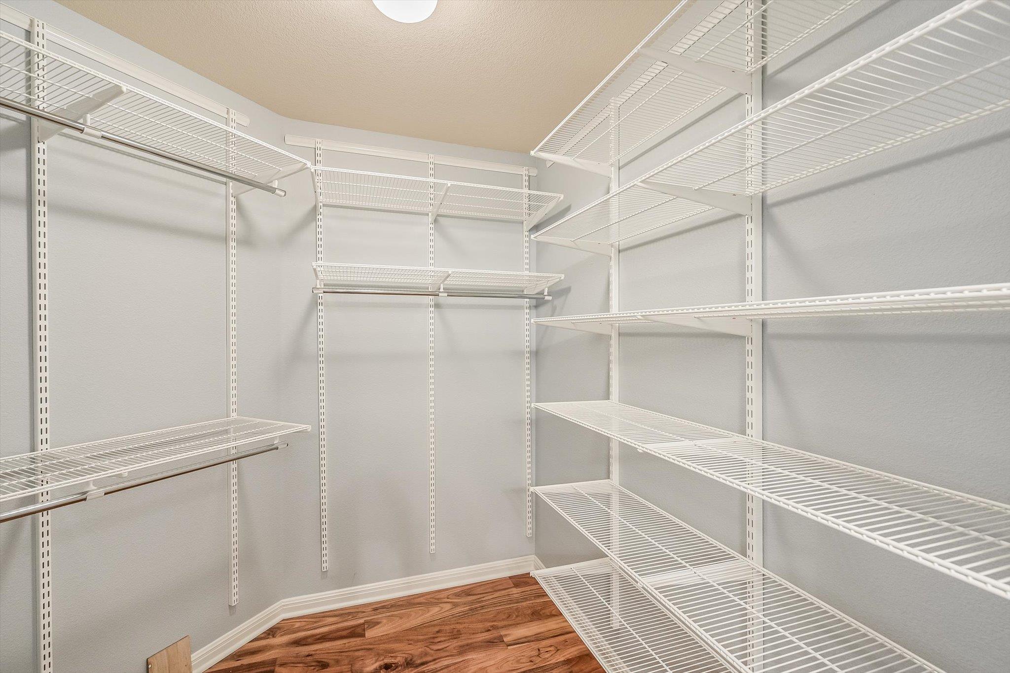Walk-in closet with white wire shelves and hanging rods above wood flooring.