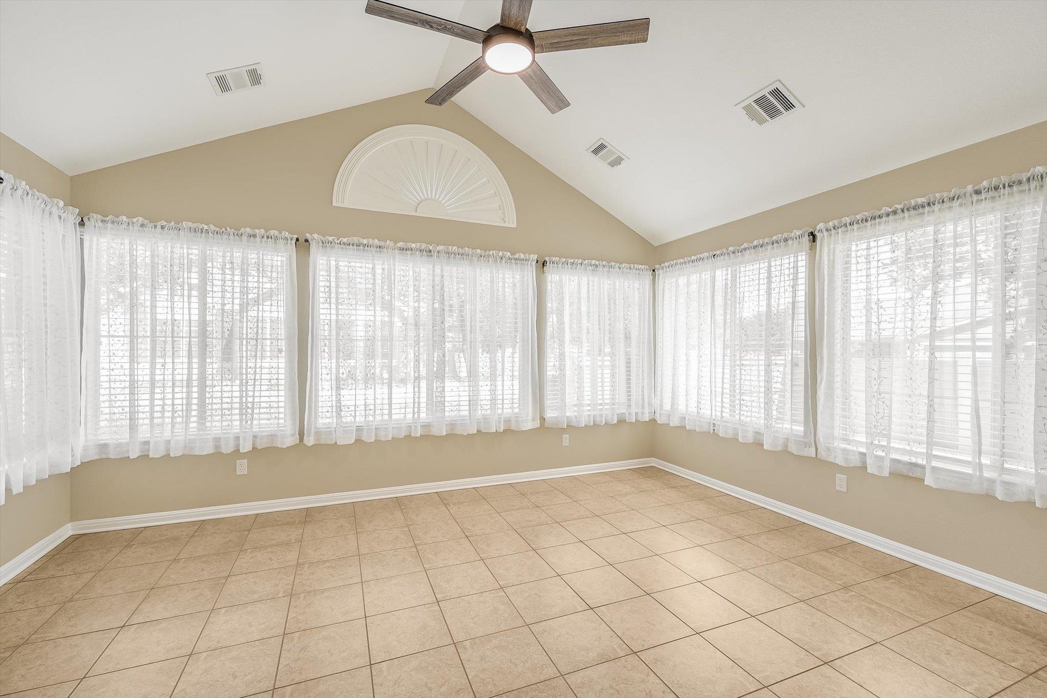 Empty sunroom with vaulted ceiling, tan tile floor, and windows along three walls.