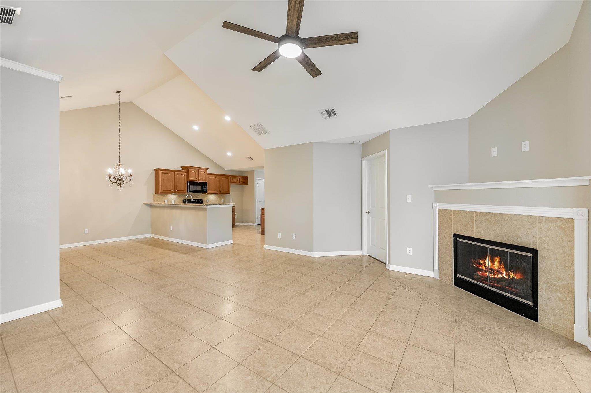 Open living room with tiled floors, vaulted ceiling, fireplace, and kitchen with wood cabinets.