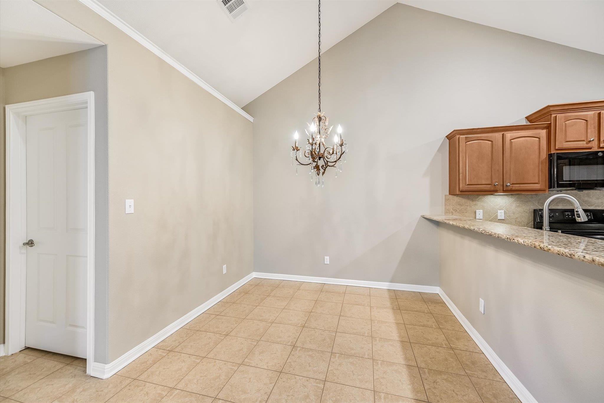 Empty dining area with a vaulted ceiling, chandelier, tiled floor, and granite breakfast bar.