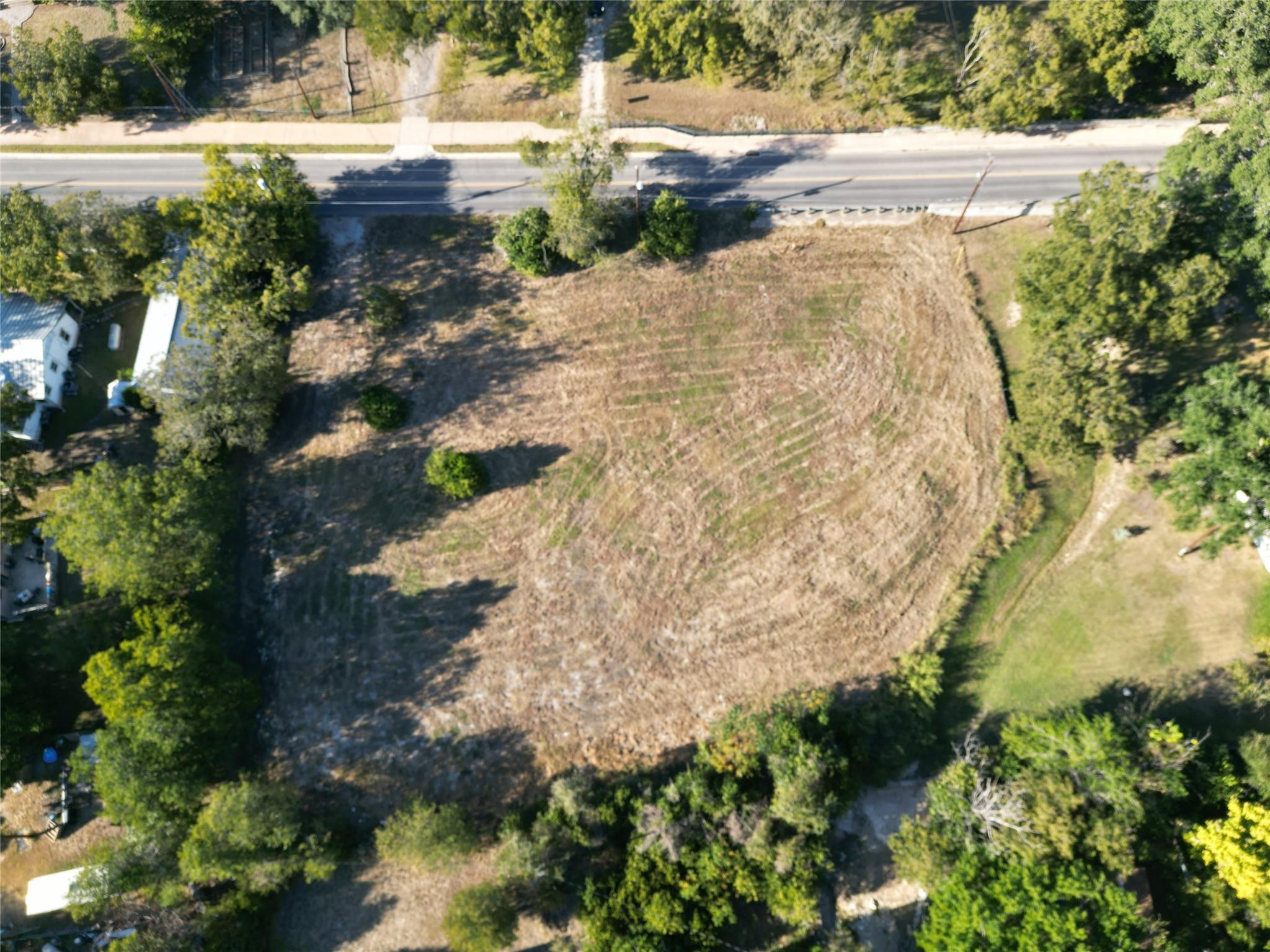 Aerial view of a cleared lot beside a paved road, bordered by mature trees.