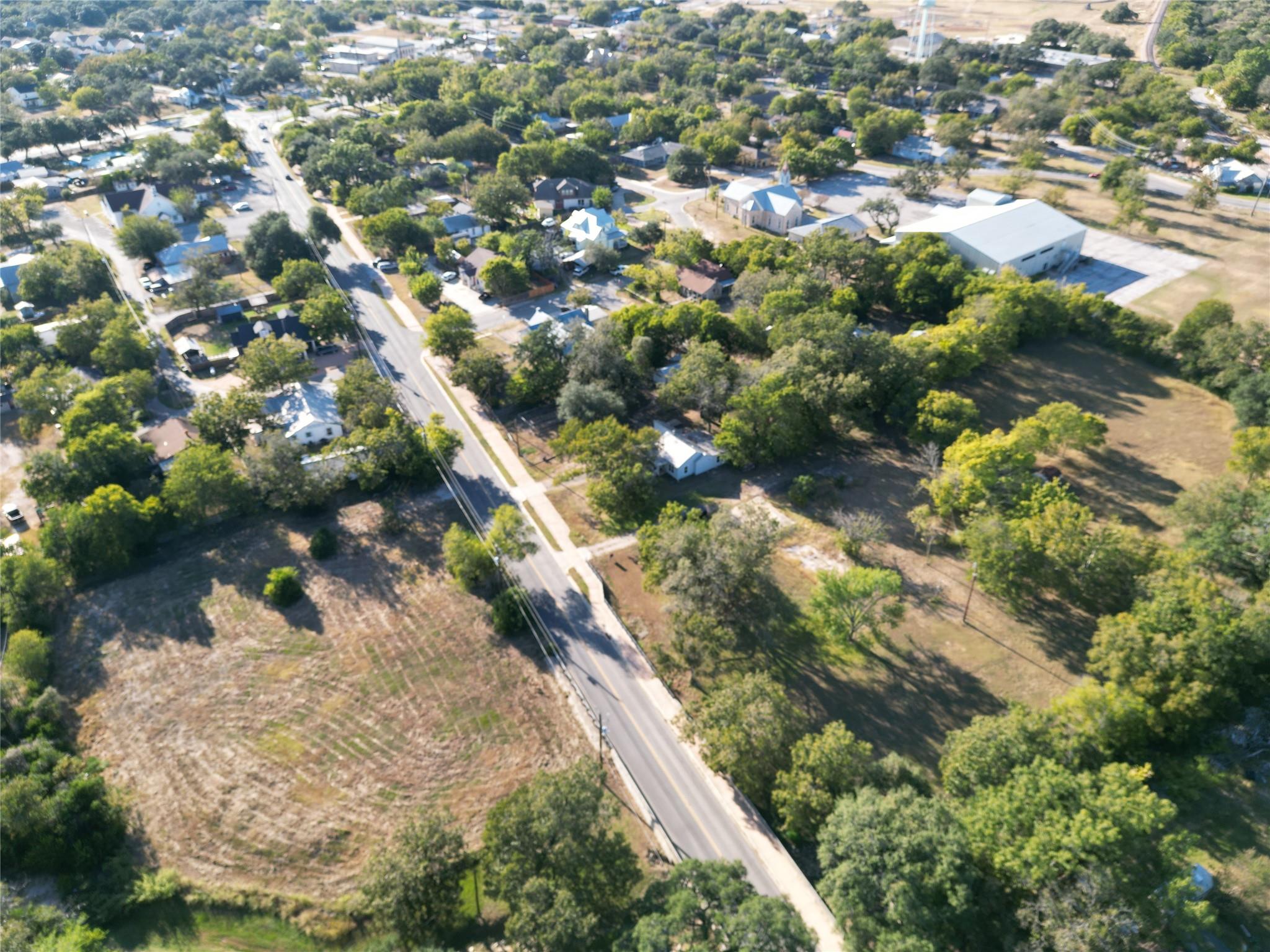 Aerial view of a tree-lined neighborhood, open lots, and a road running between homes.
