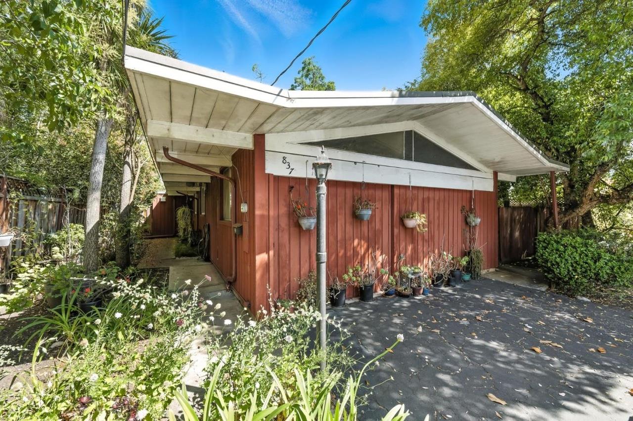 Red wood-sided house with a broad white roof, triangular clerestory windows, and a leafy garden.