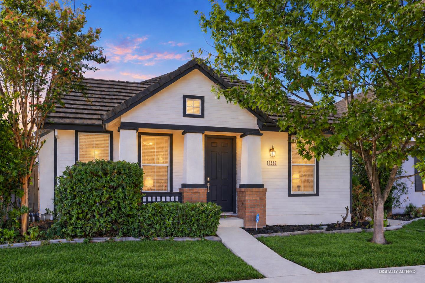 White house with dark trim and tiled roof, framed by trees, with a walkway to the front door.