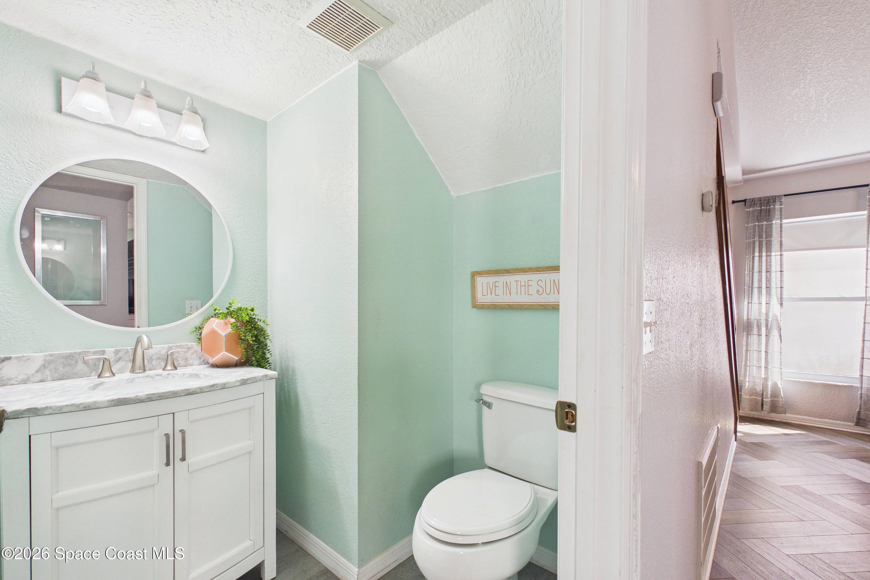 Mint-green bathroom with a marble-top vanity, oval mirror, and toilet alcove.