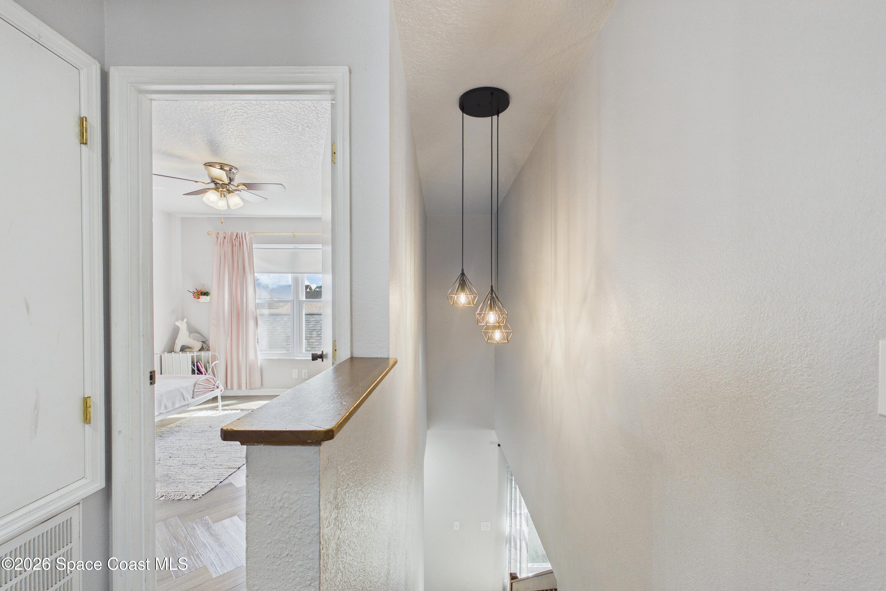 Upstairs landing overlooking a stairwell, with geometric pendant lights and a bedroom visible through the doorway.