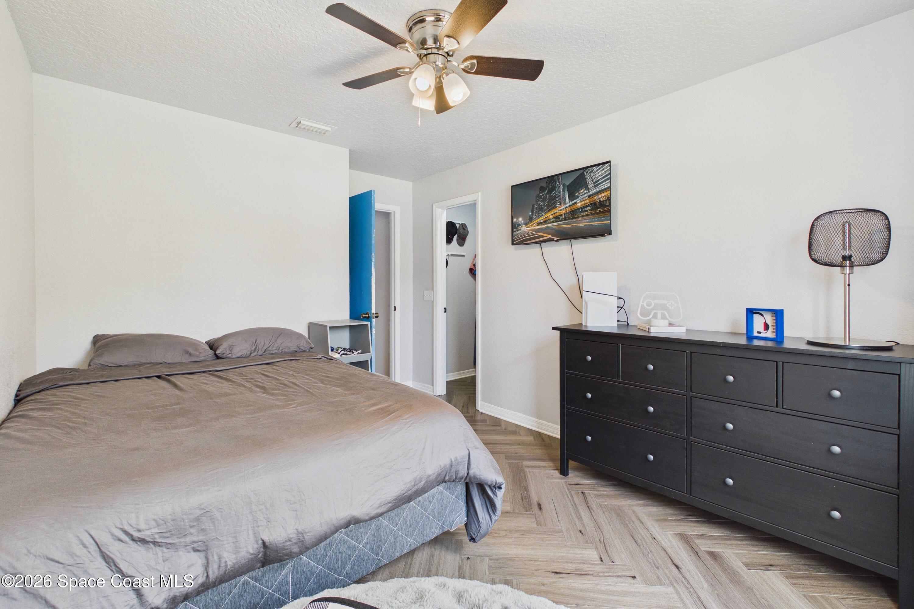 Bedroom with a gray bed, dark dresser, ceiling fan, and herringbone wood flooring.
