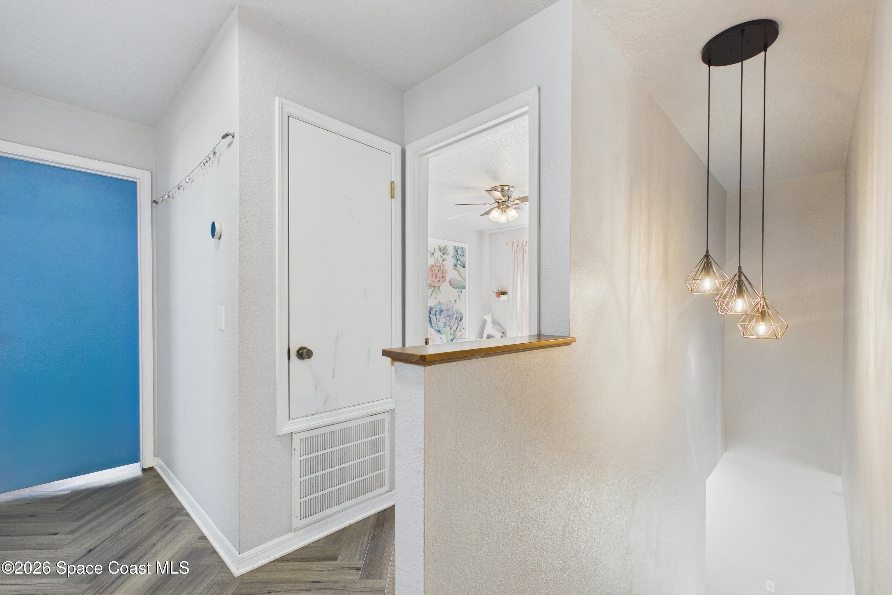 Entryway with a blue front door, wood-look flooring, and geometric pendant lights above the stairwell.