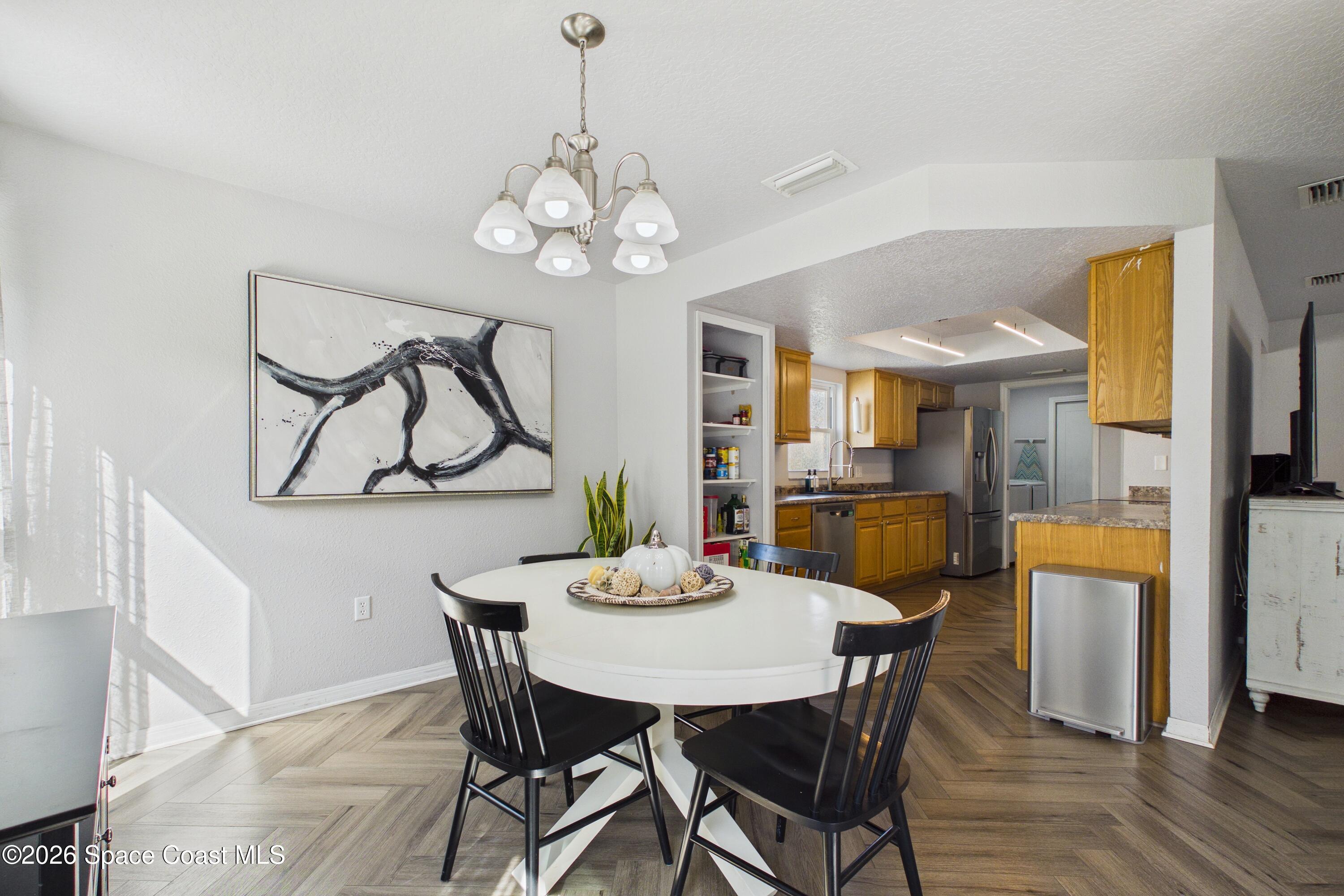 Dining area with a round white table and black chairs opening into a wood-cabinet kitchen.