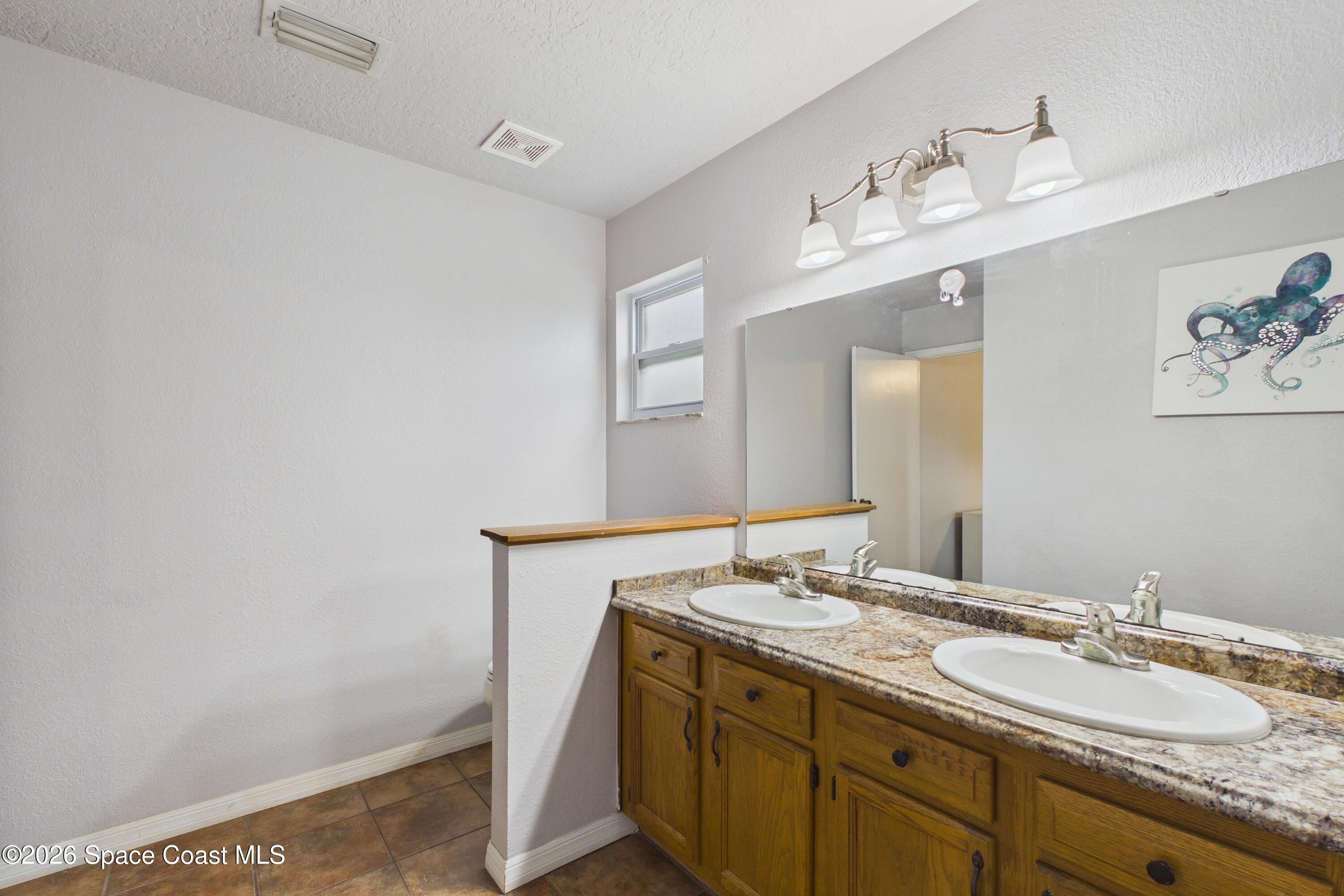 Bathroom with a double-sink wood vanity, mottled countertop, large mirror, and octopus artwork.