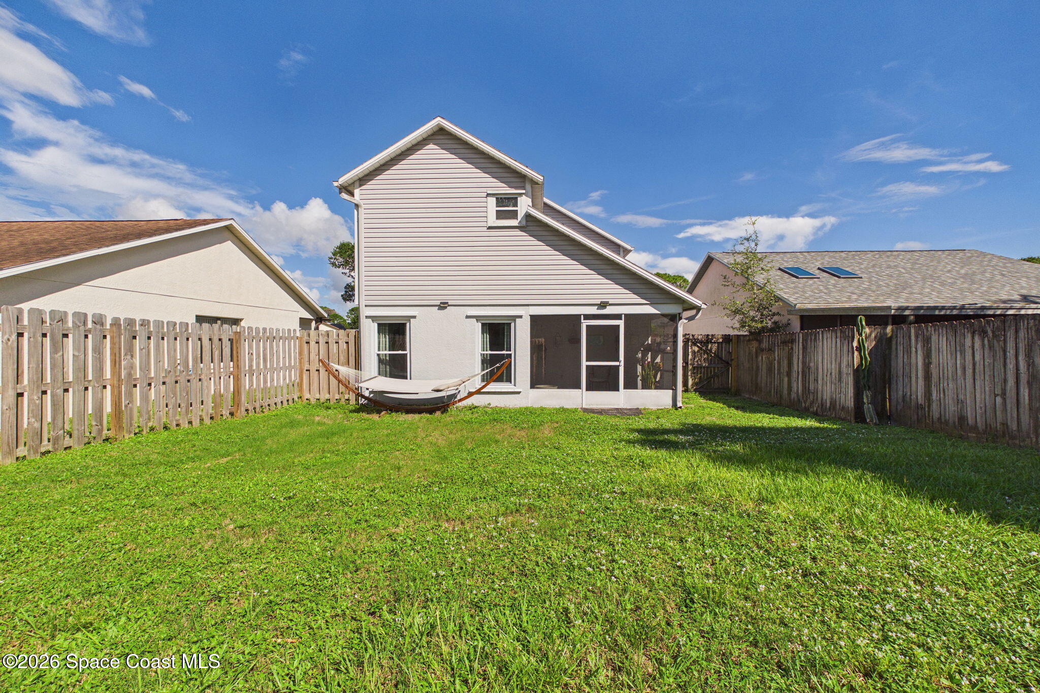 Rear of a white two-story house with a screened patio, hammock, and fenced grassy yard.