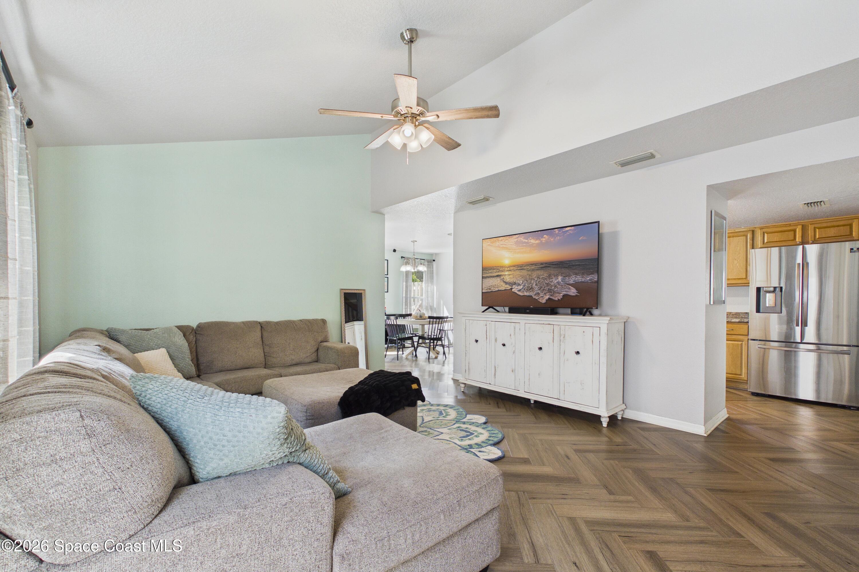 Furnished living room with a large sectional, ceiling fan, and open view toward the dining area and kitchen.