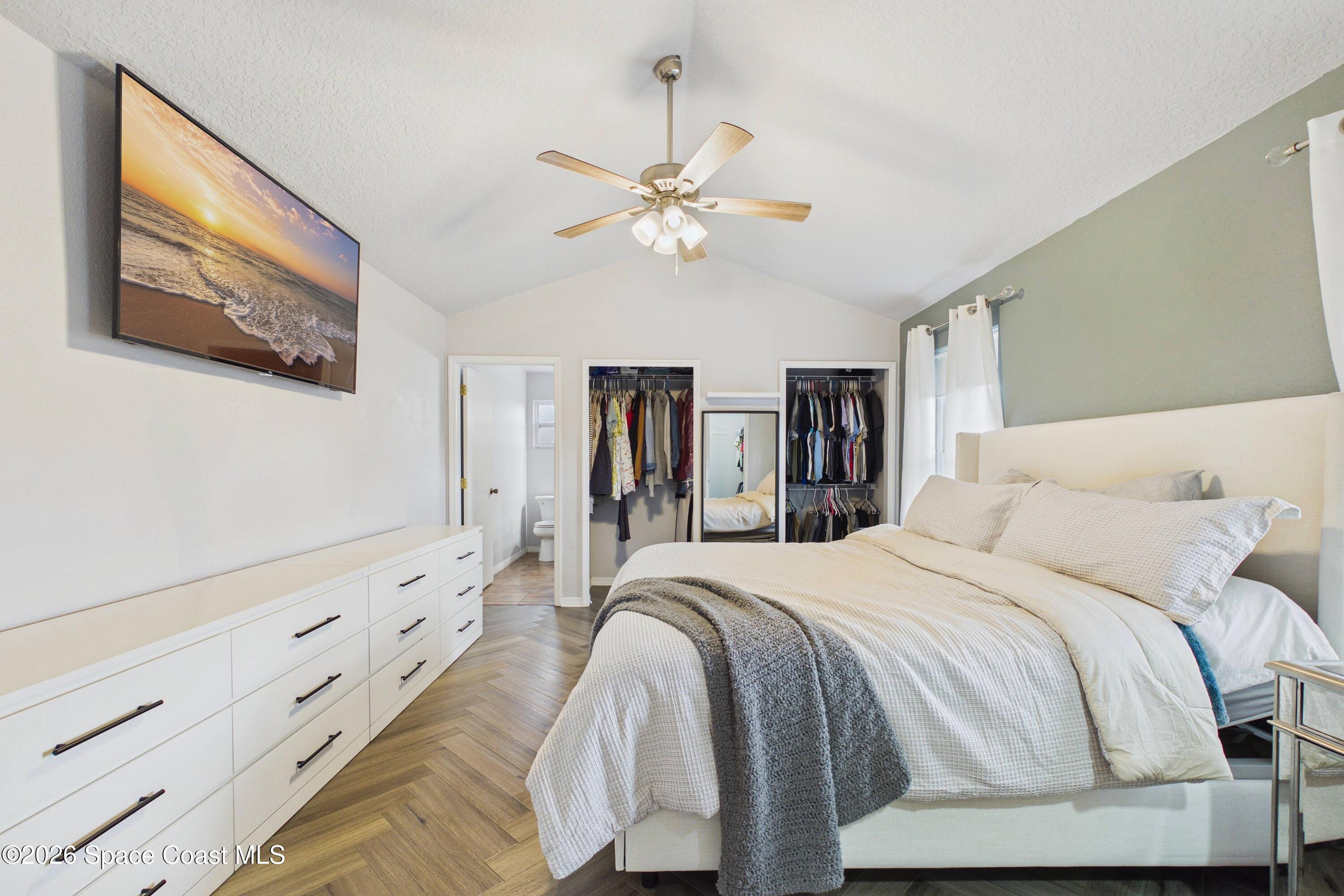 Furnished bedroom with a vaulted ceiling, white bed, dresser, and two open closets.