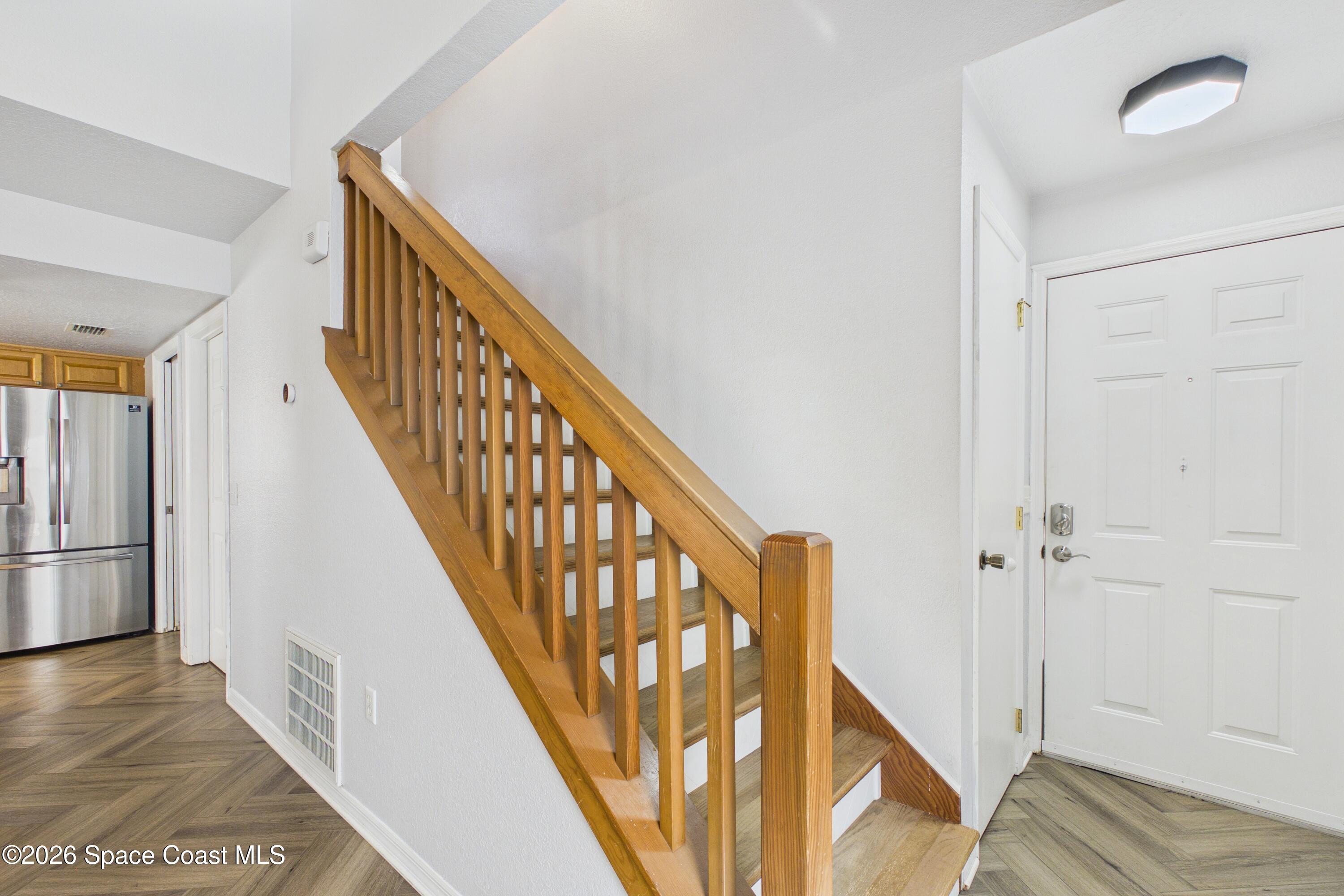 Entryway with a wooden staircase, white front door, and herringbone flooring.