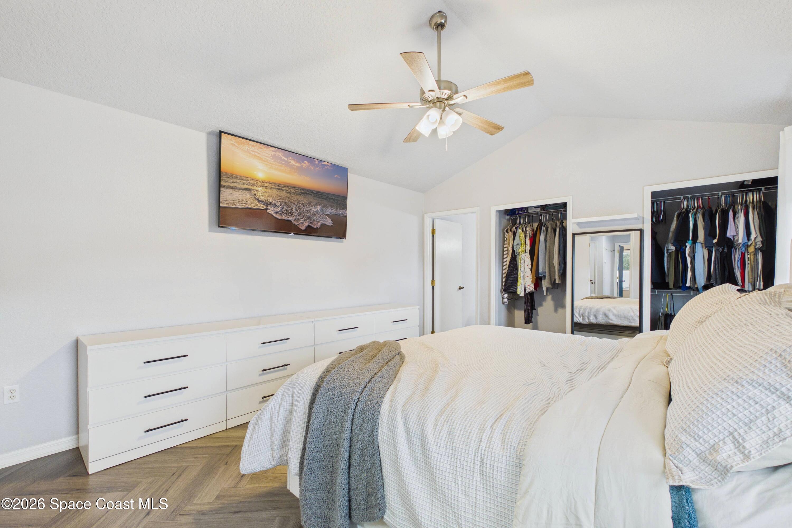 Furnished bedroom with a white bed, ceiling fan, dresser, and two open closets.