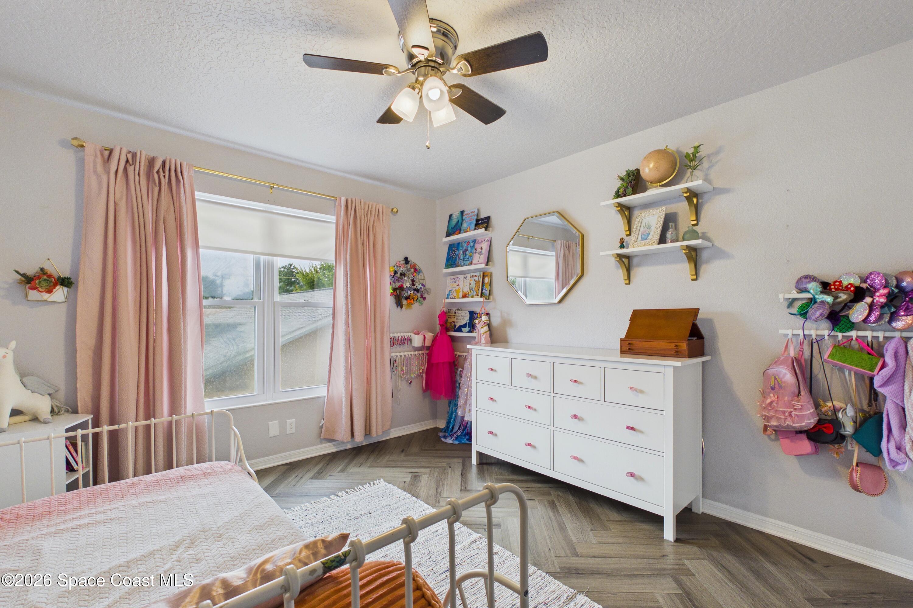 Bedroom with a white metal bed, pink curtains, and a white dresser beneath shelves.