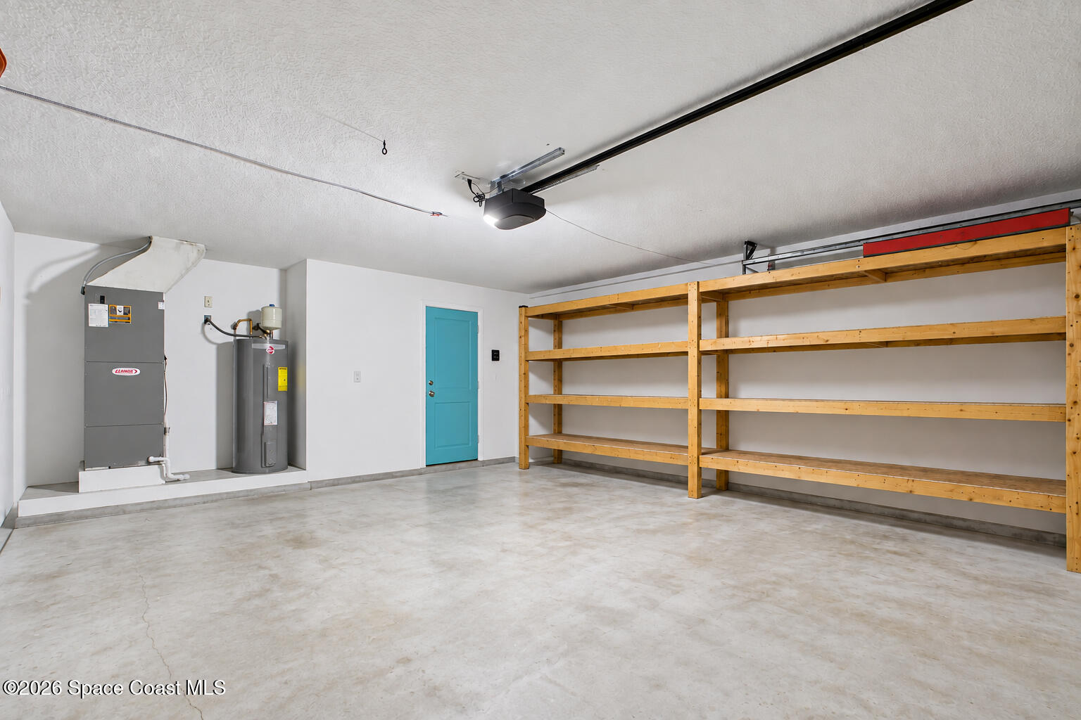 Garage with long wooden storage shelves, a blue side door, and utility equipment.