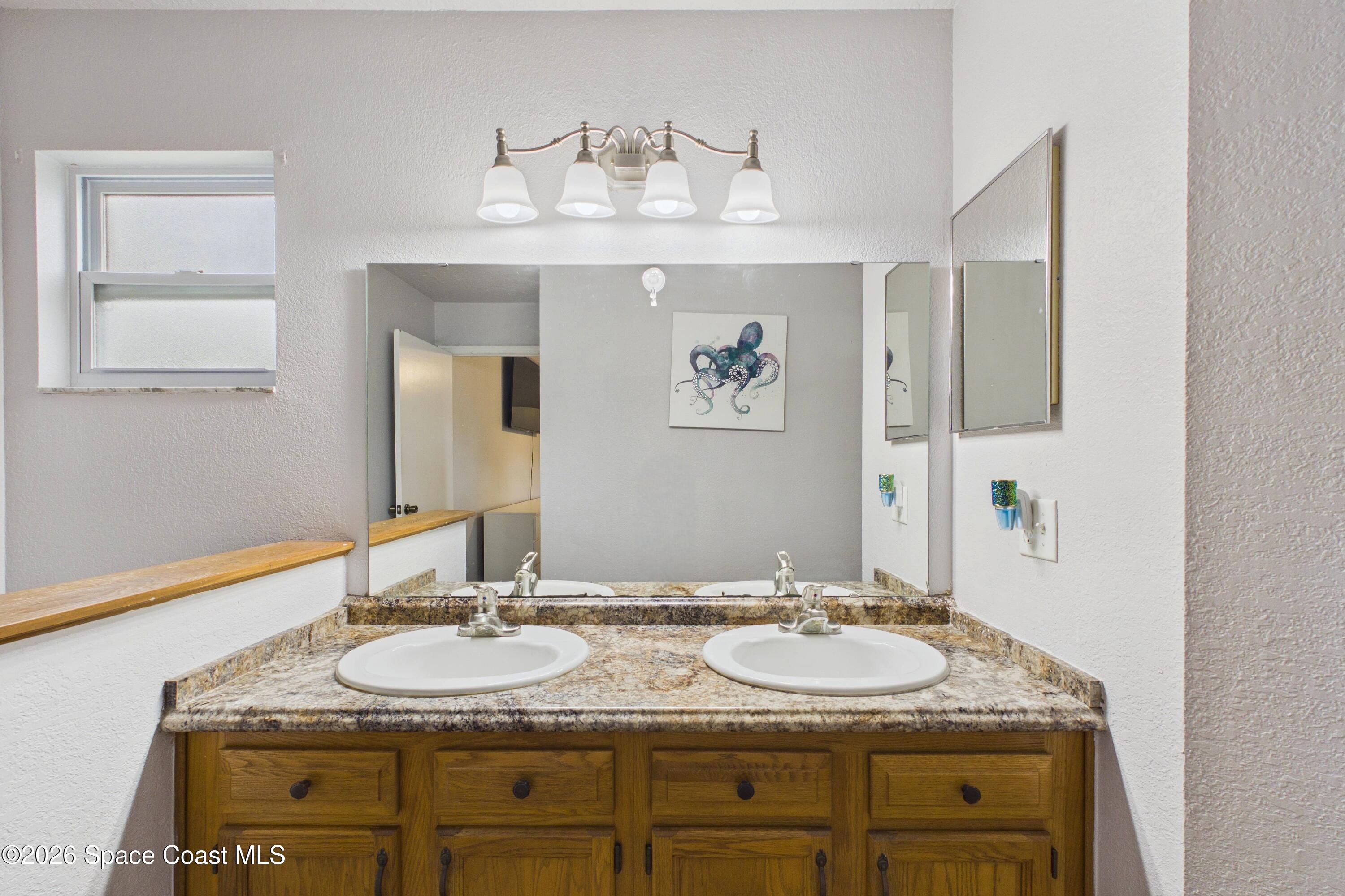 Bathroom with a double-sink vanity, mottled stone counter, and warm wood cabinetry.