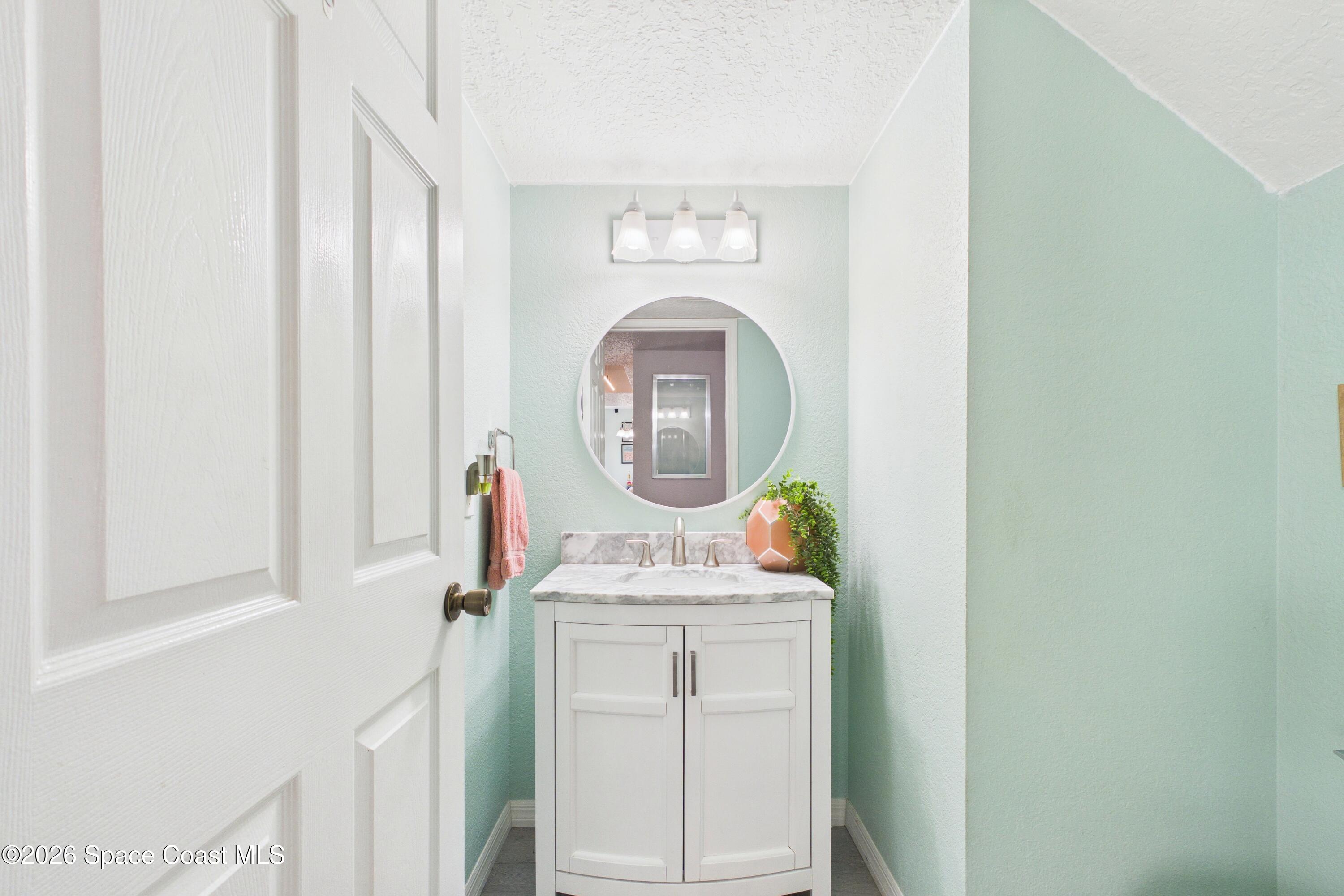 Bathroom vanity with a round mirror, marble-look counter, and pale mint walls.