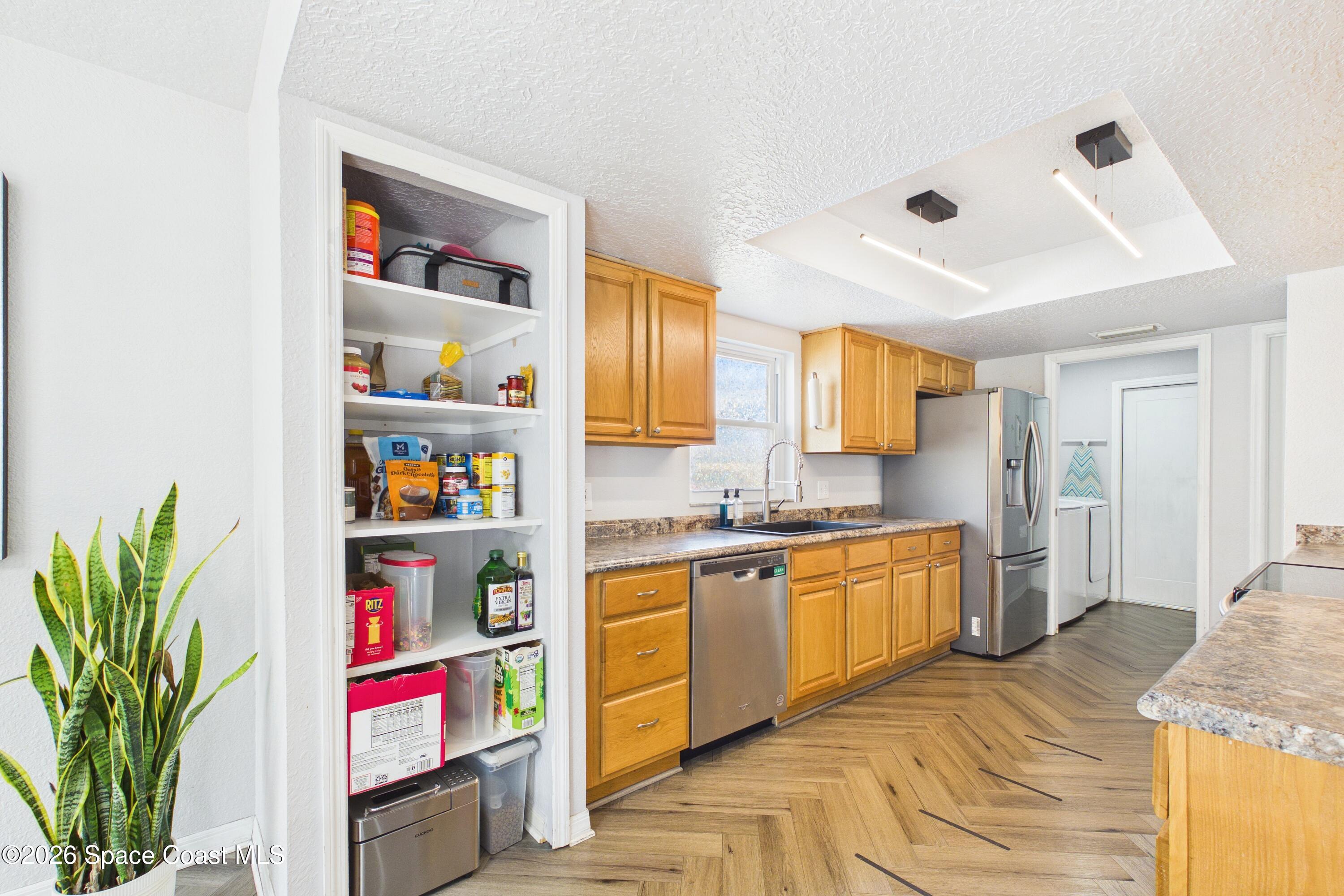 Kitchen with honey-colored cabinets, stainless steel appliances, stocked pantry, and herringbone wood flooring.