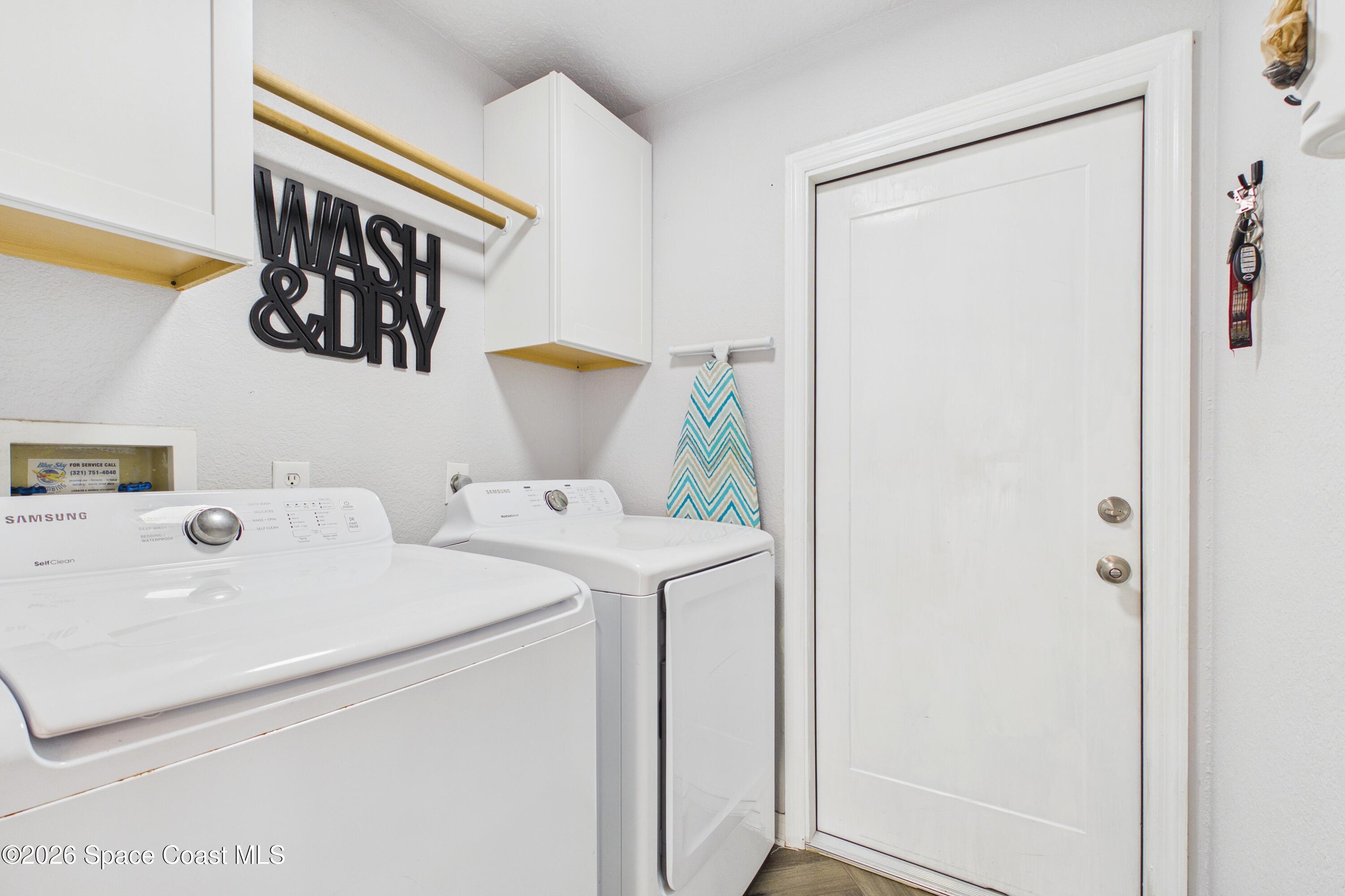 Laundry room with white washer and dryer, wall cabinets, and a black “WASH & DRY” sign.