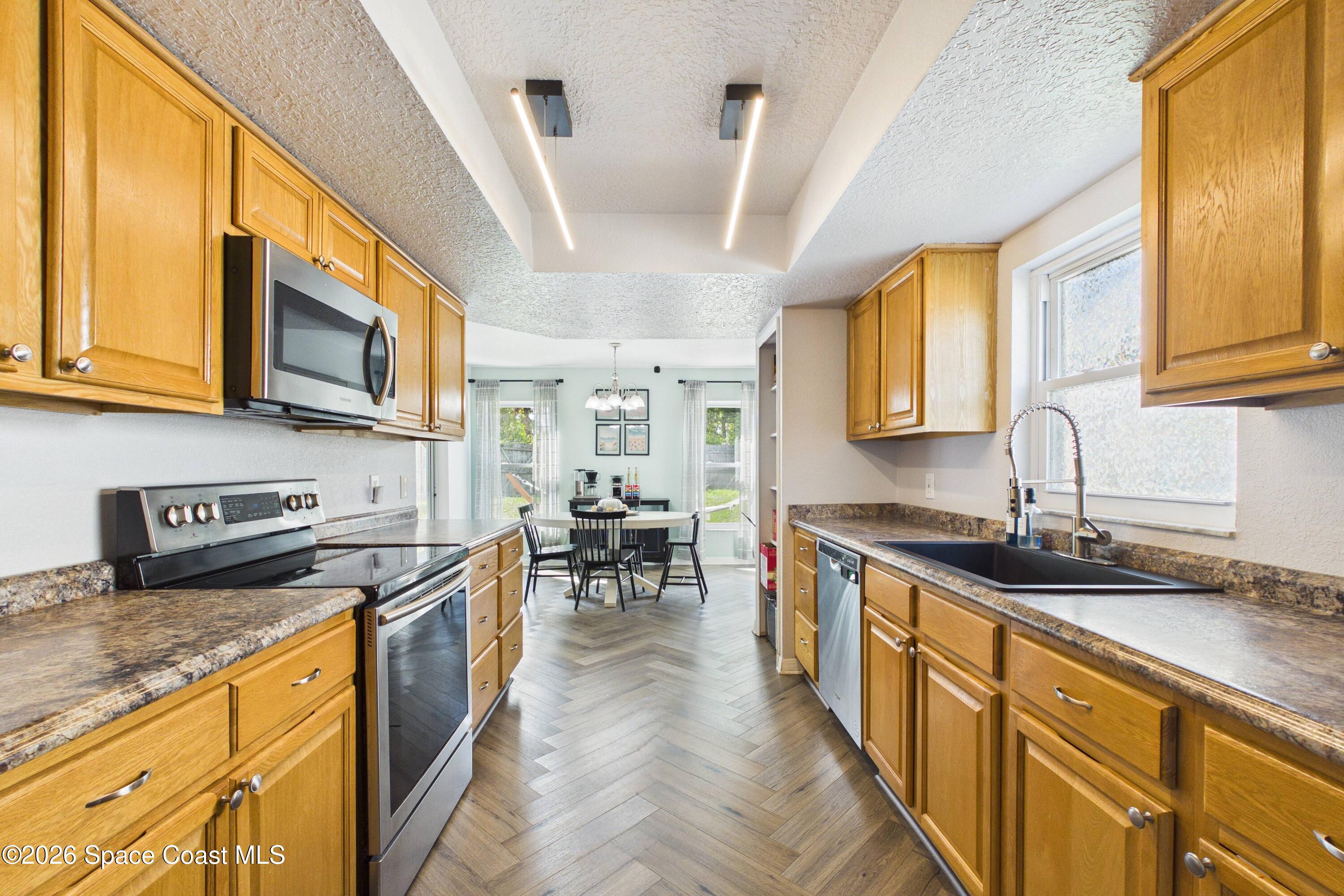 Kitchen with honey-colored cabinets, stone-pattern counters, stainless appliances, and a dining table by the windows.
