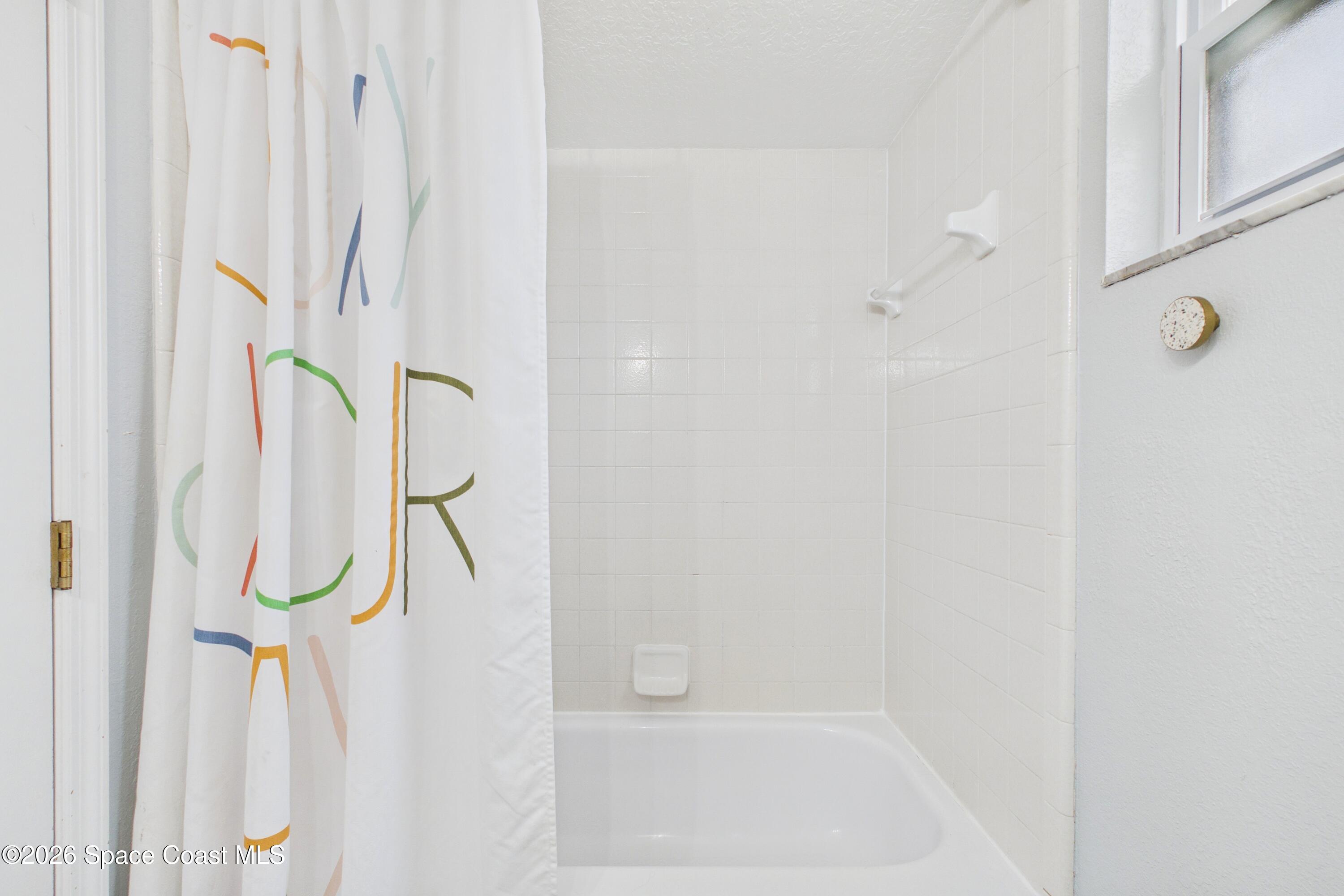 Bathroom with a white tiled bathtub, colorful patterned shower curtain, and frosted window.