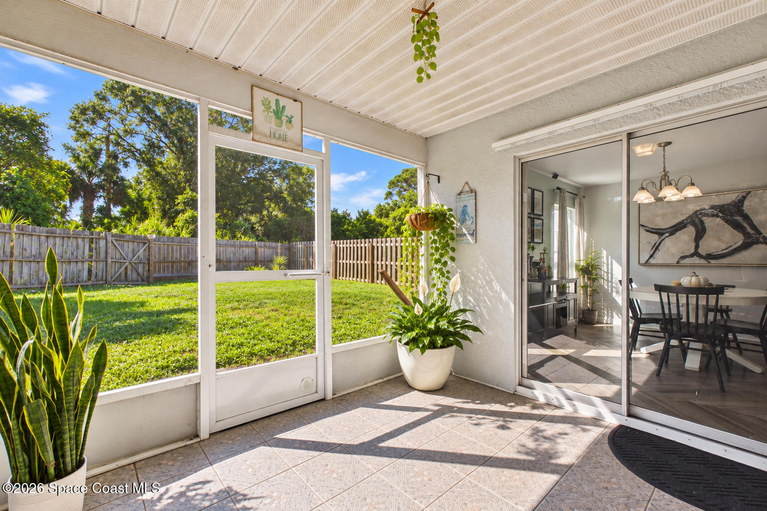 Screened patio with tiled flooring, hanging plants, and views of the fenced backyard.