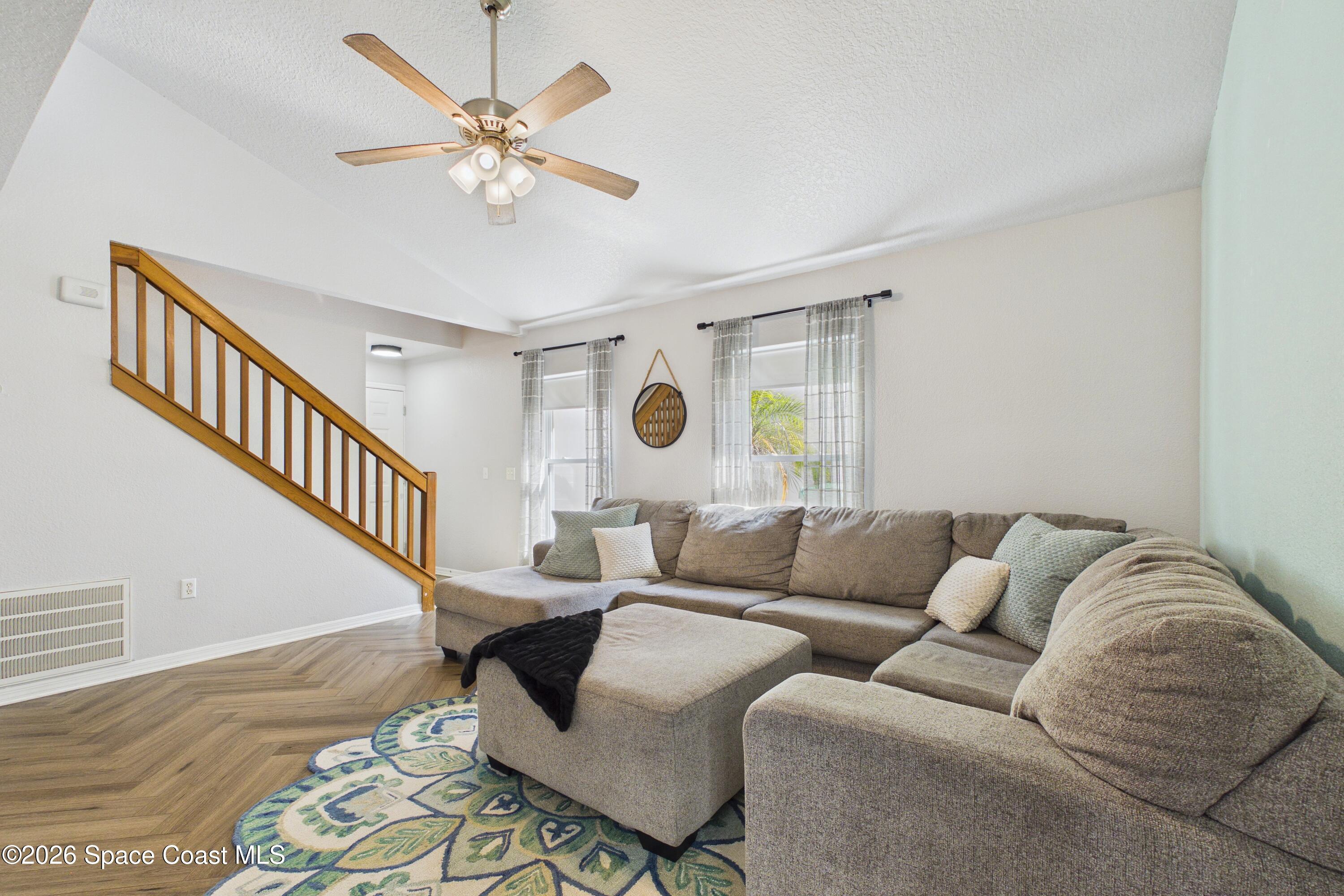 Living room with a gray sectional, patterned rug, and wooden staircase with railing.