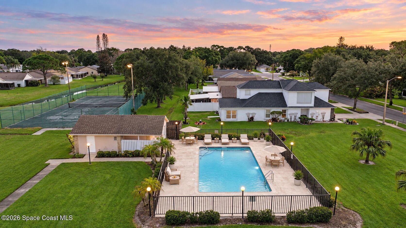 Aerial view of a home’s fenced pool patio with outdoor seating at dusk.