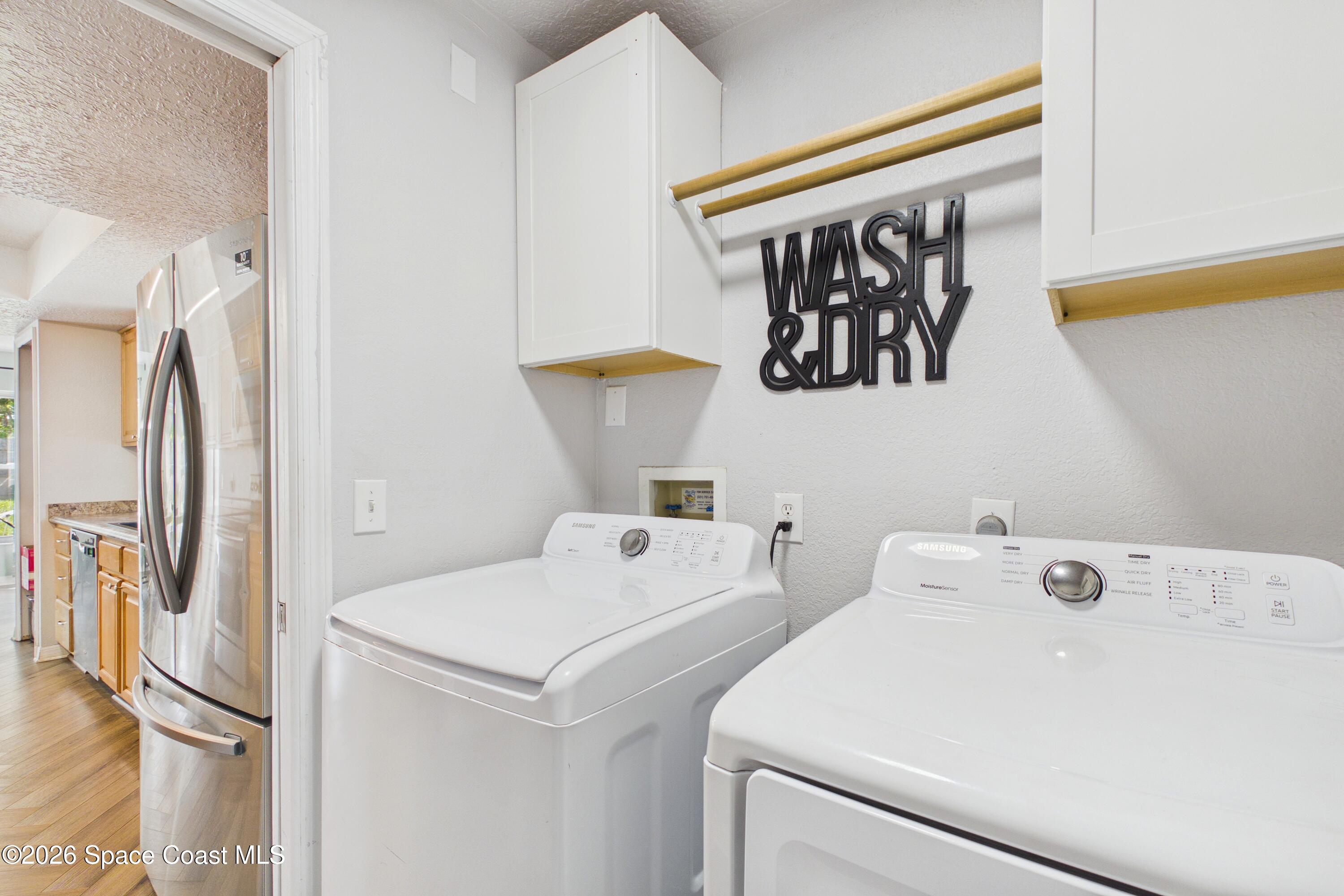 Laundry room with white washer and dryer, overhead cabinets, and wooden hanging rods.