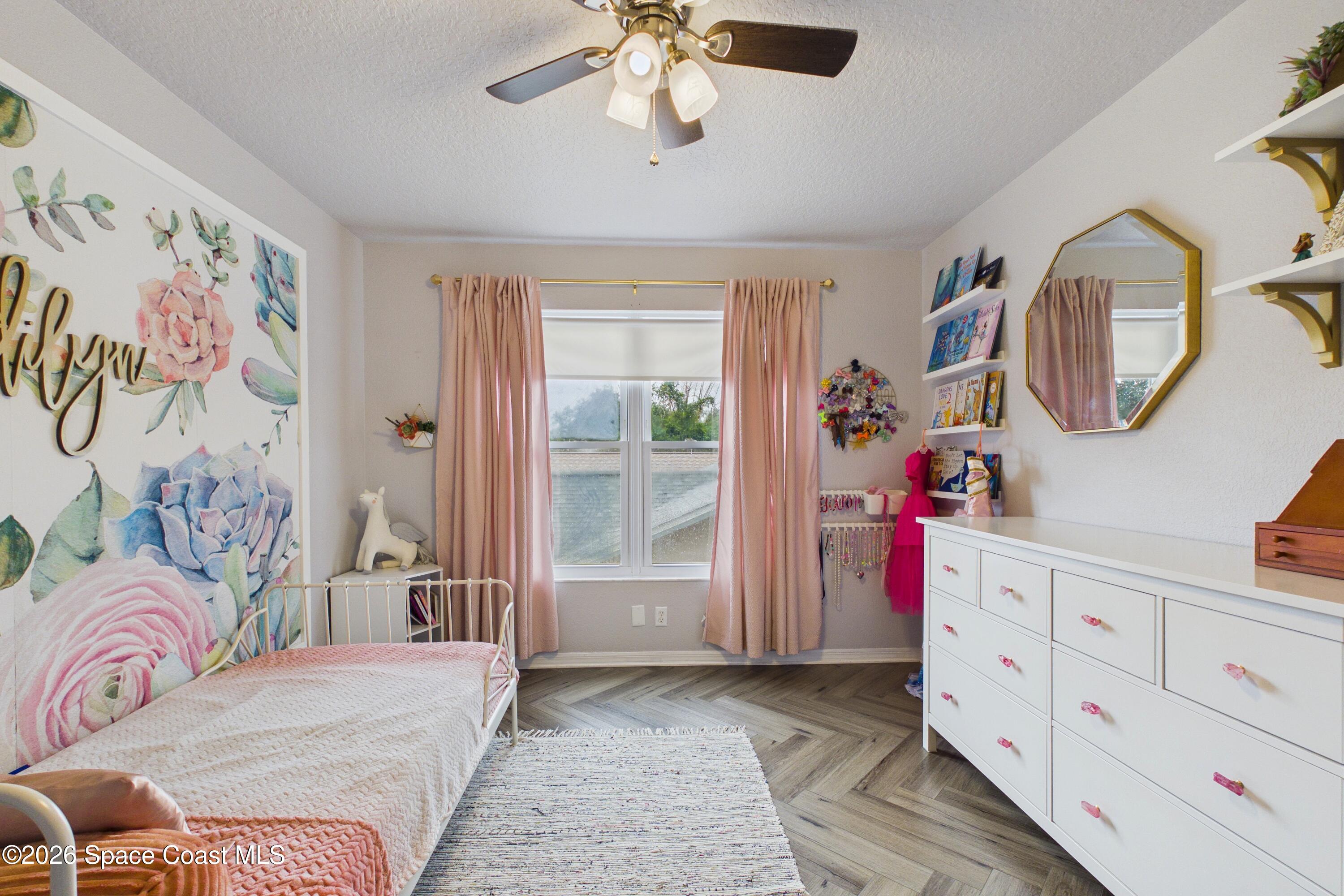 Bedroom with a floral mural, white metal bed, pink curtains, and white dresser.