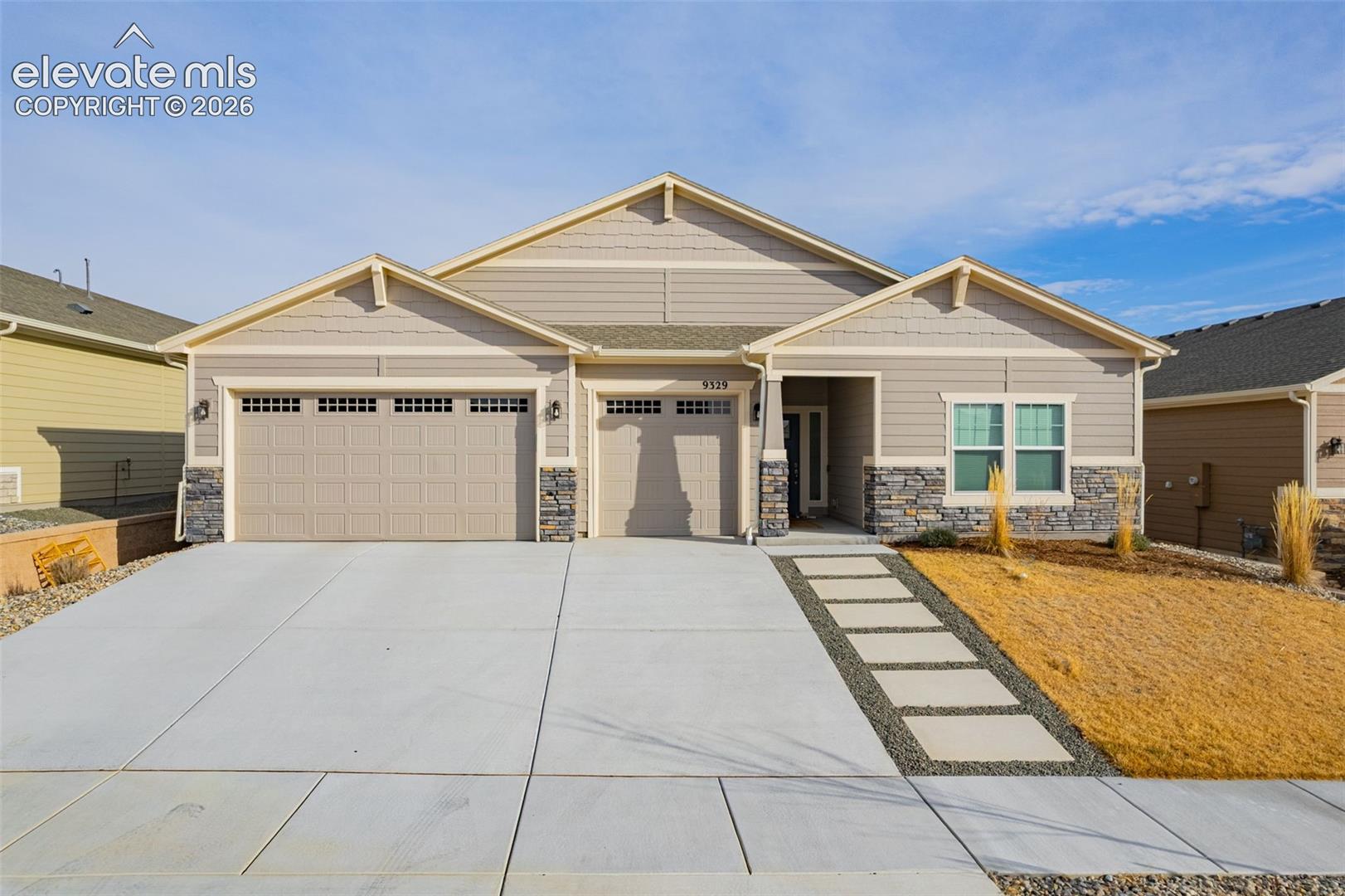 Beige single-story home with stone accents, a two-car garage, and a broad concrete driveway.