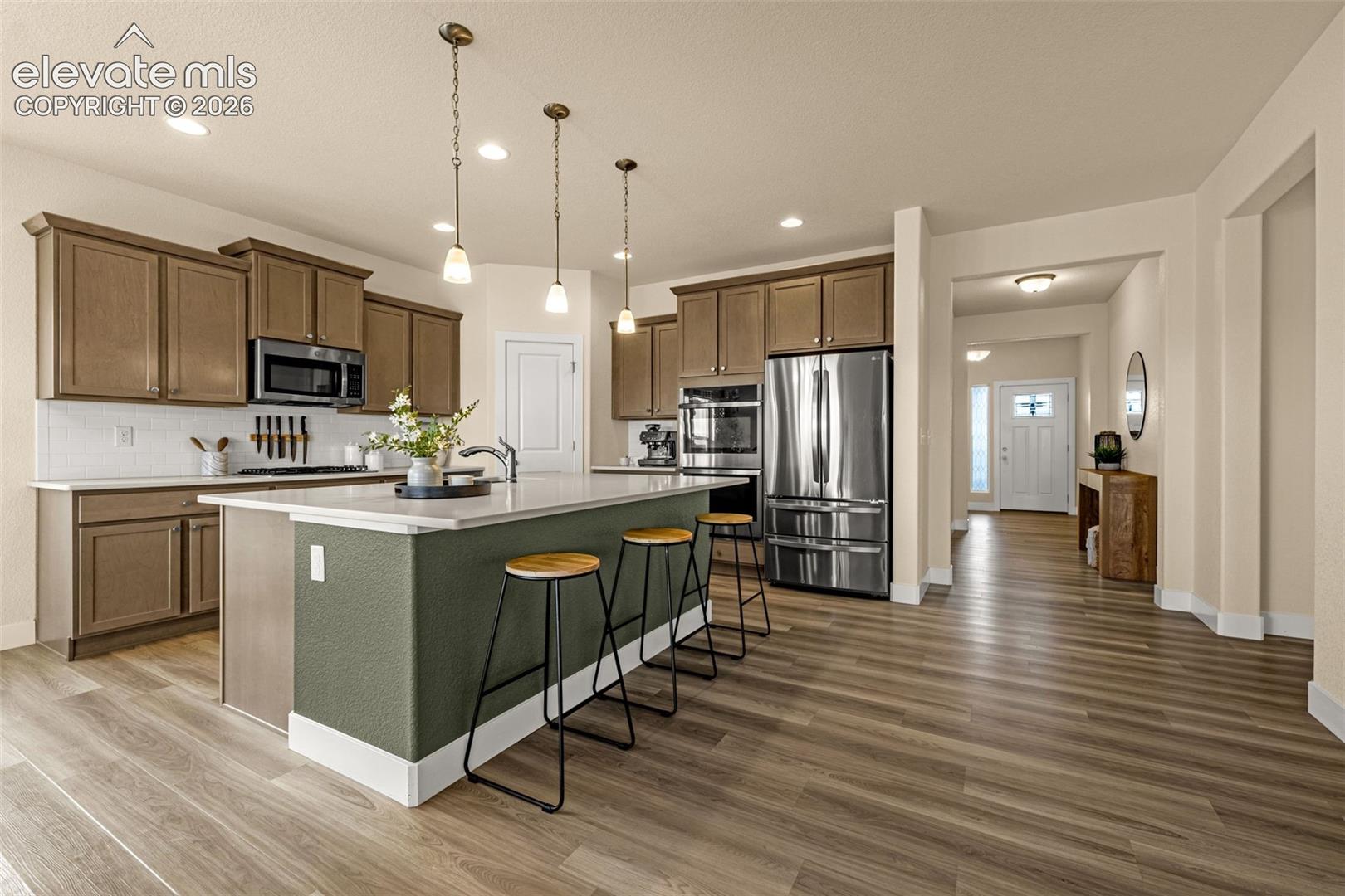 Open kitchen with brown cabinets, stainless appliances, and a green island with three stools.