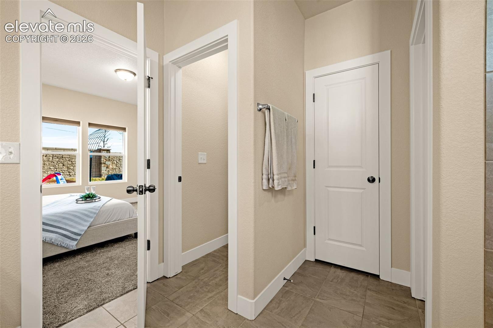 Tiled hallway with white doors and towel bar, opening to a bedroom with a neatly made bed.