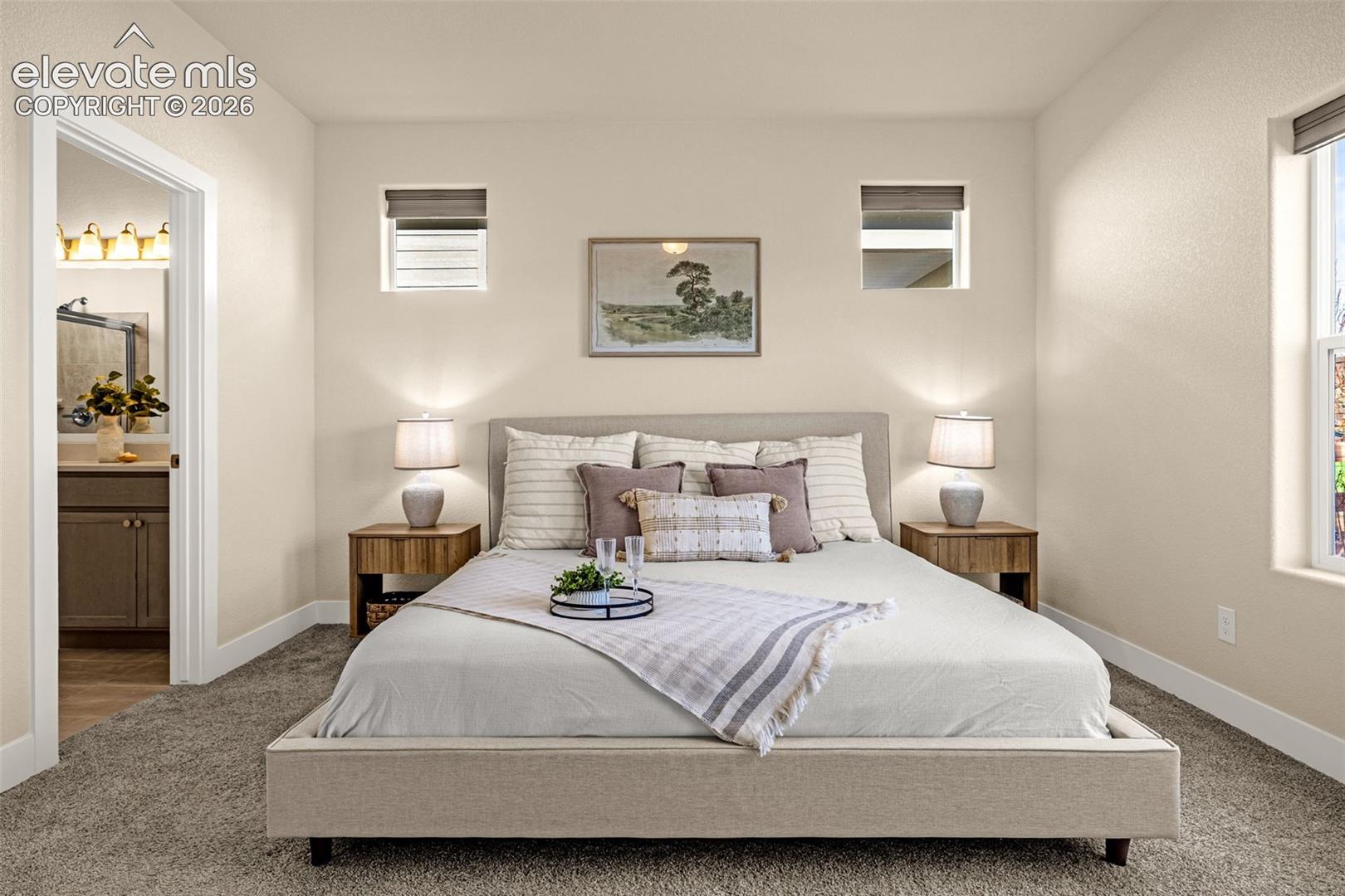 Staged bedroom with a large upholstered bed, matching nightstands, and a doorway to the bathroom.