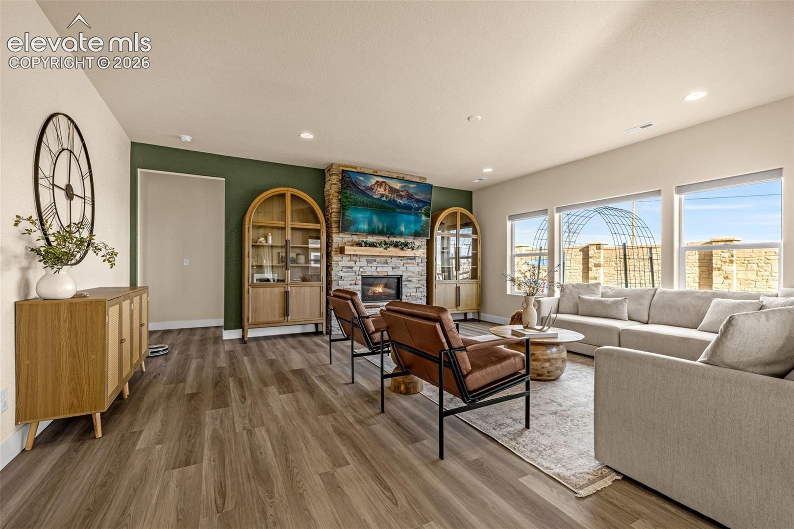 Living room with a stone fireplace, arched wood cabinets, and large windows.