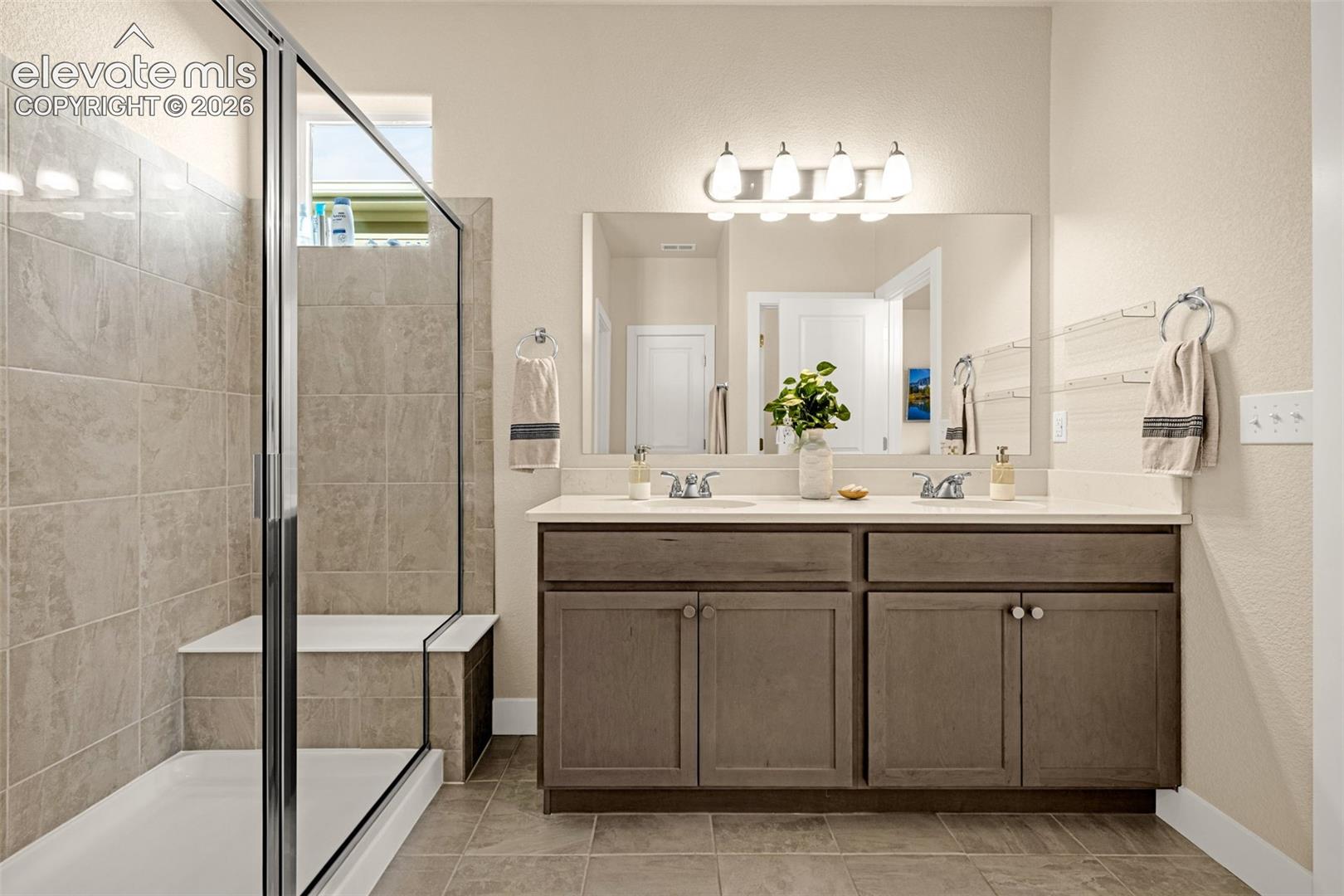 Bathroom with a glass-enclosed tub and shower beside a double-sink vanity.