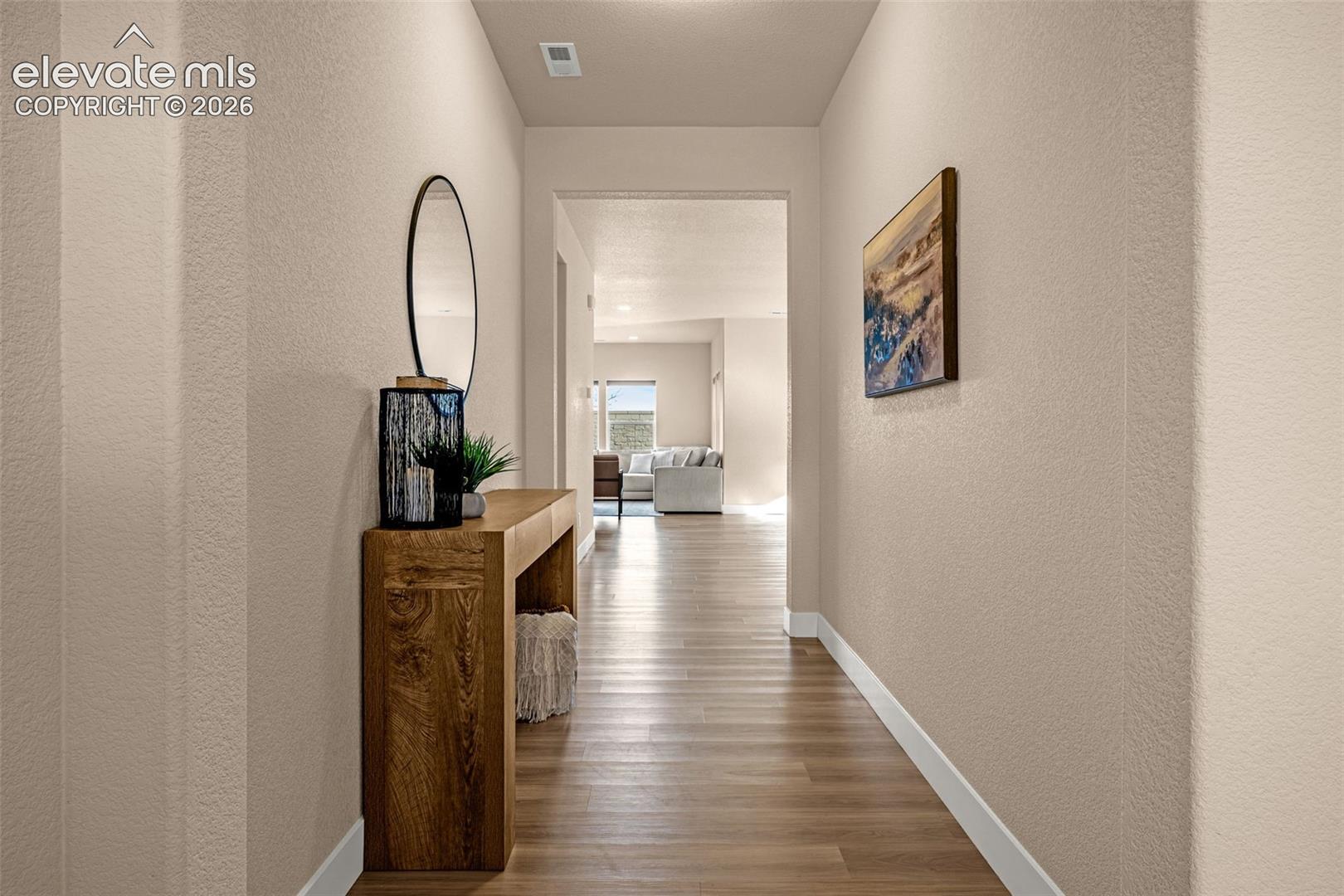 Furnished hallway with a wooden console, oval mirror, and view into a living room.