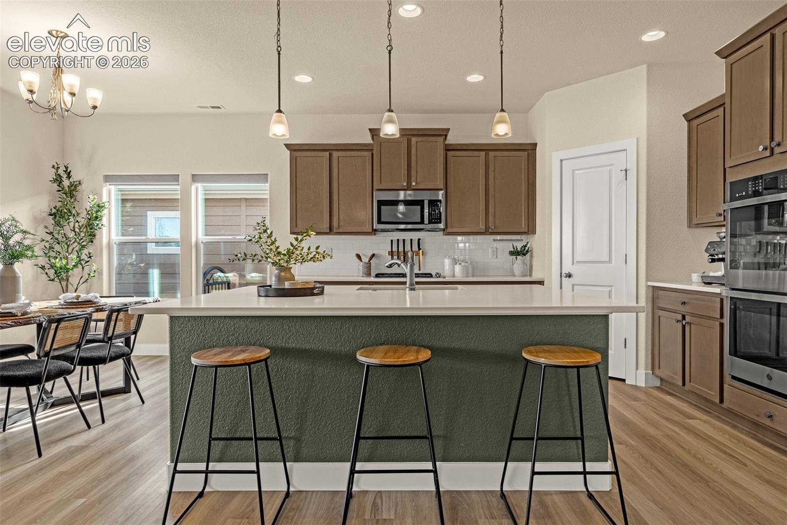Kitchen with a large green island, three stools, brown cabinetry and a dining area by the windows.