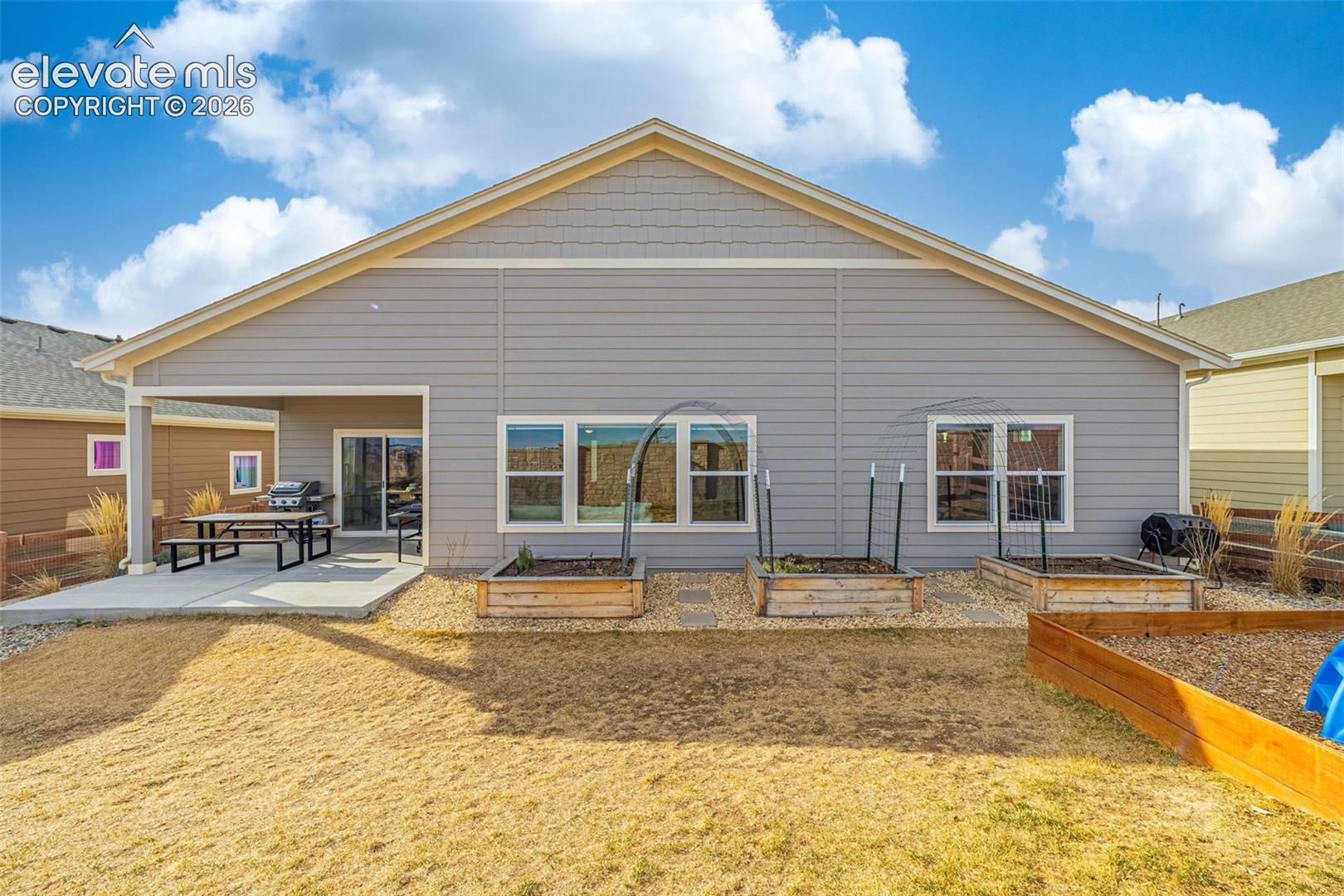 Rear of a gray-sided home with a covered patio and raised garden beds.