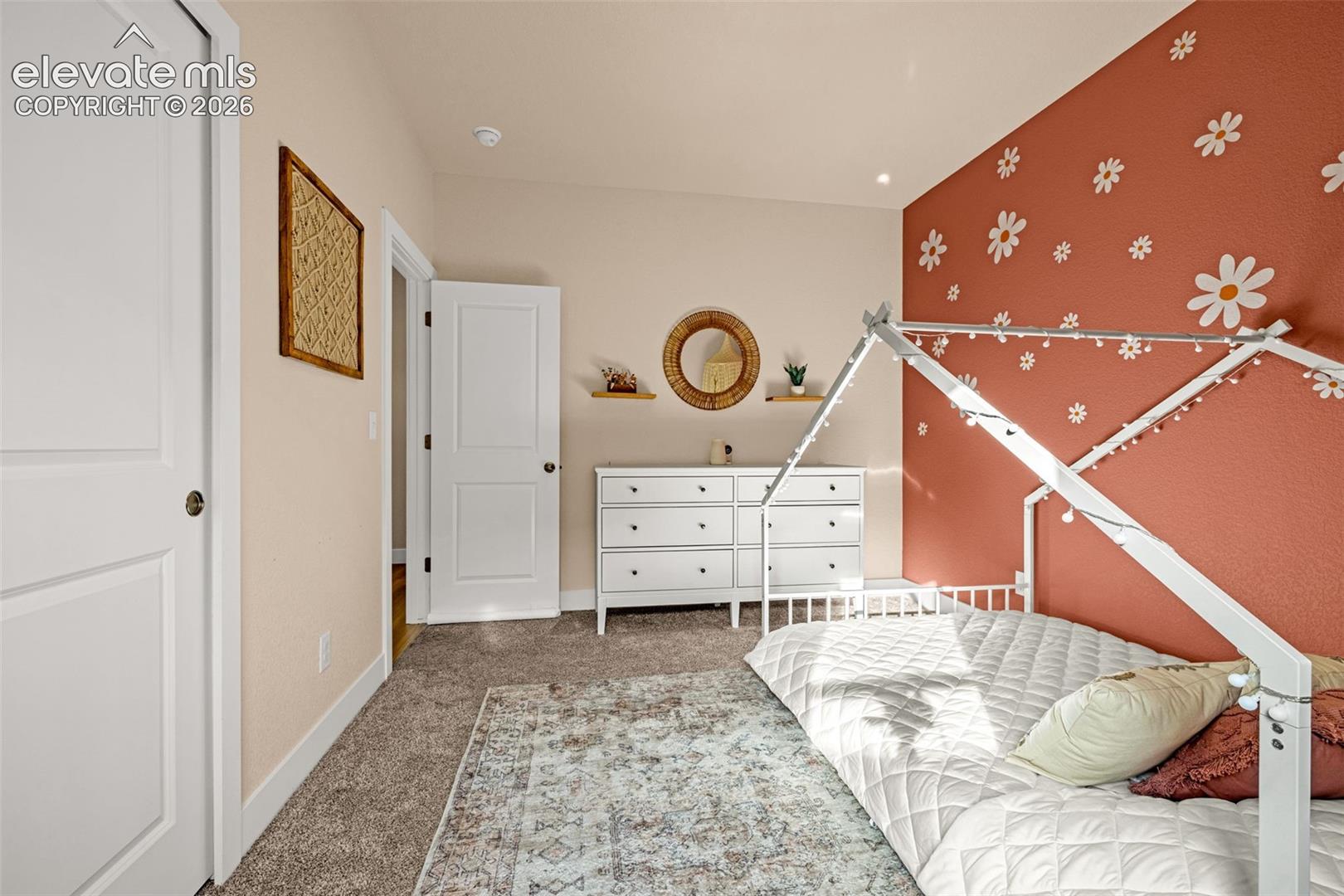Bedroom with a white house-frame bed and a rust-colored wall covered in white flower decals.