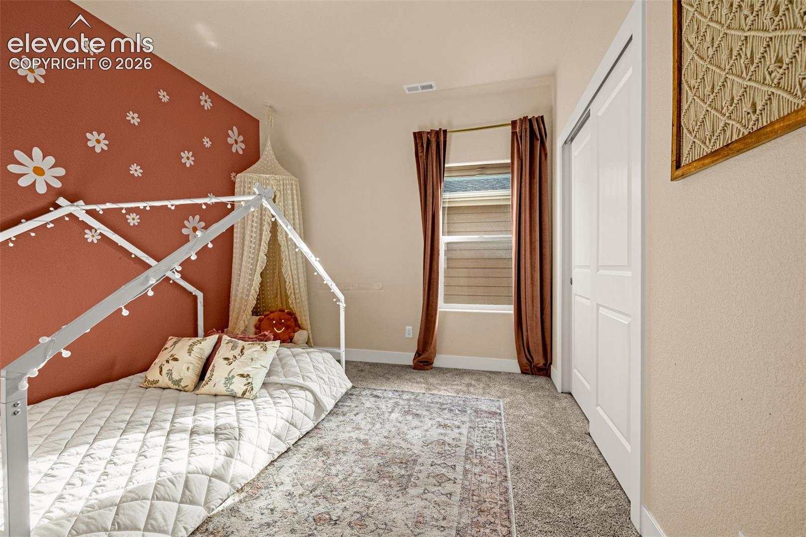 Bedroom with a white house-frame bed, floral accent wall, and curtained window.