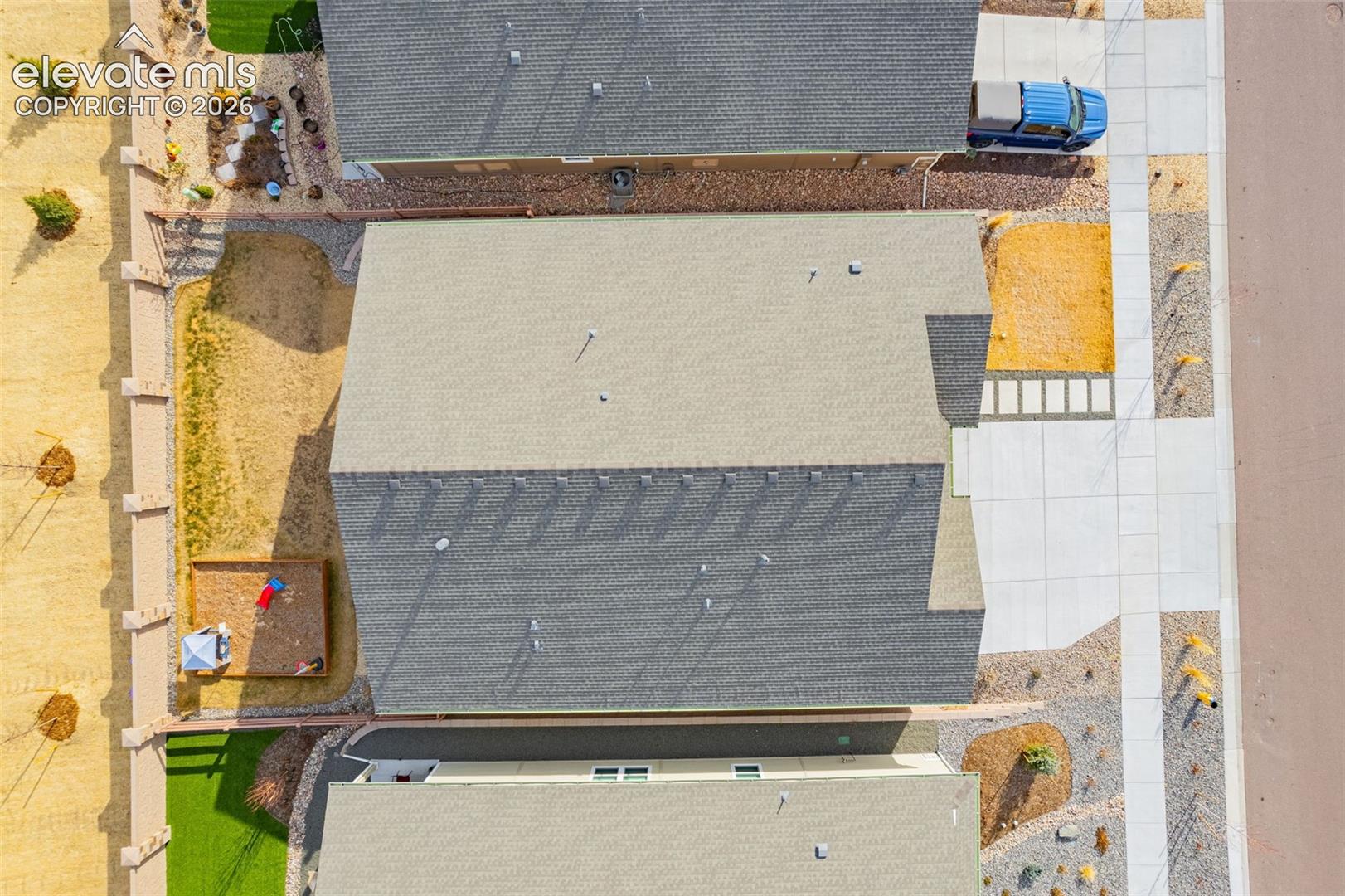 Aerial view of the home’s shingle roof, fenced yard, and neighboring driveways.
