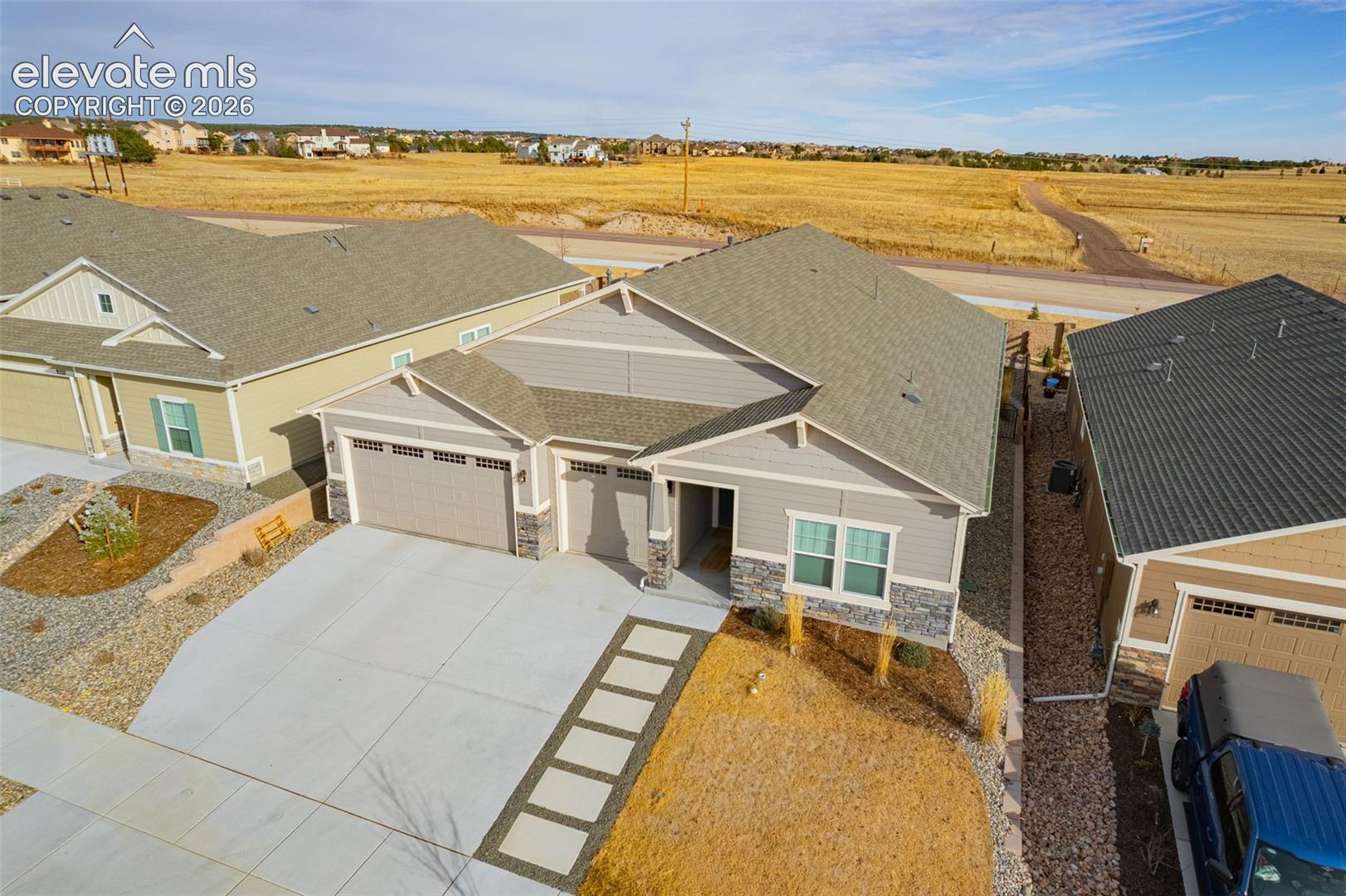 Aerial view of a single-story home with a wide driveway beside an open field.