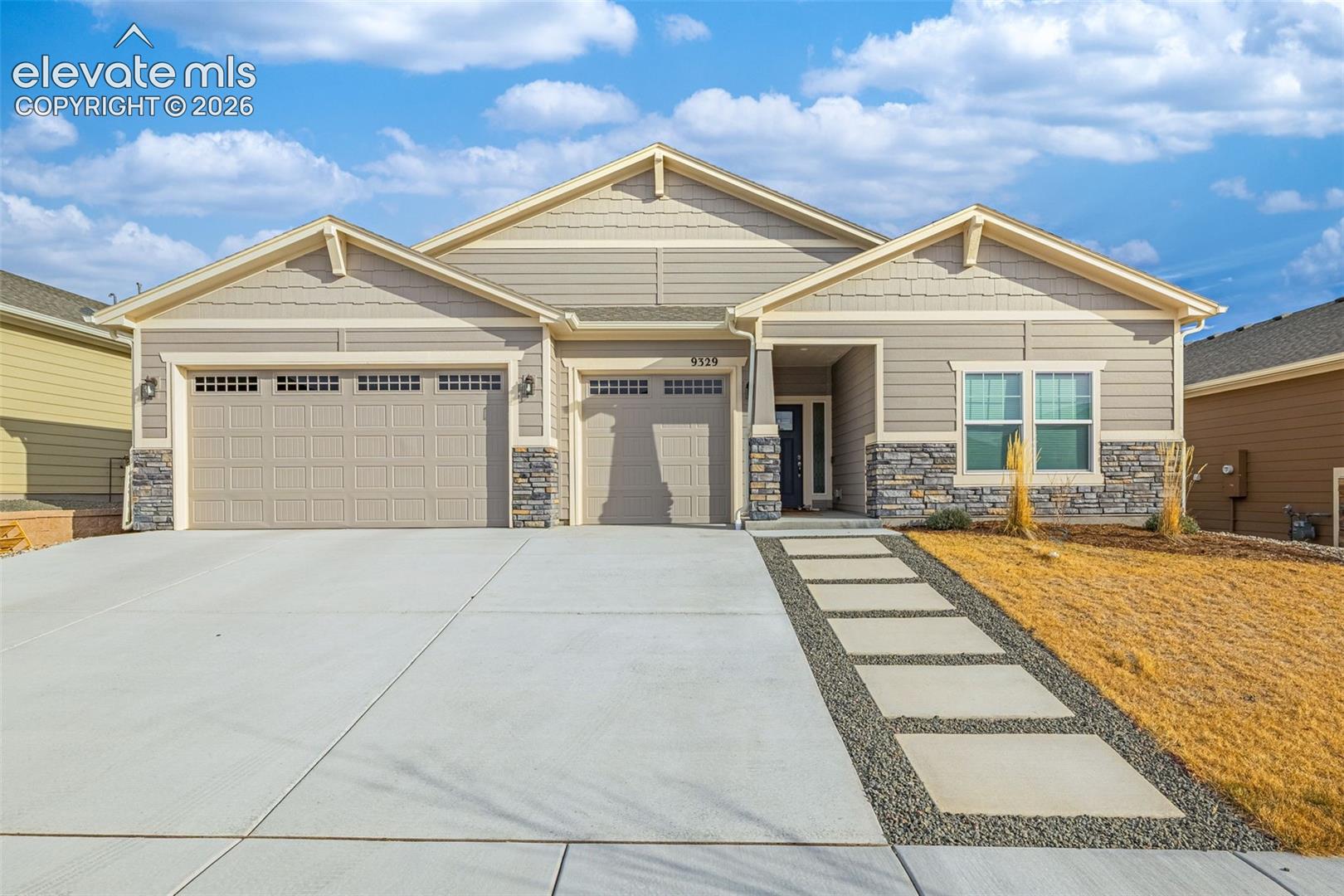 Front of beige single-story home with stone accents, three-car garage, and wide driveway.
