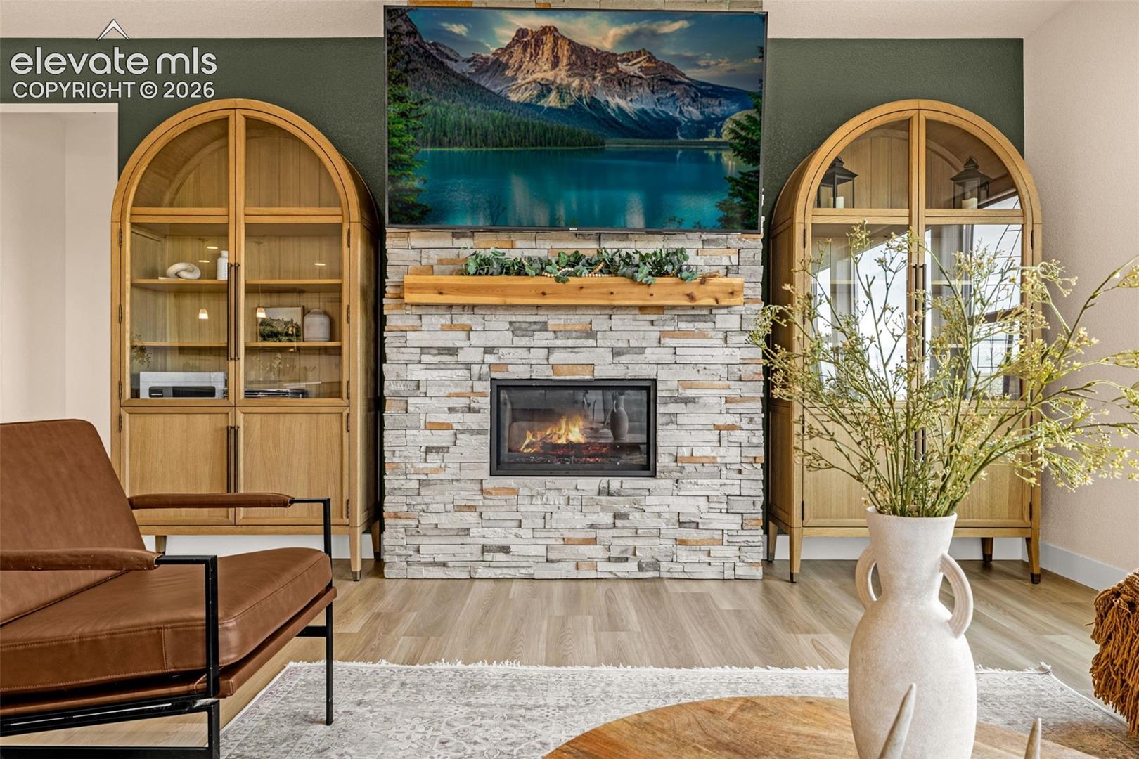 Living room with a stacked-stone fireplace, arched wood cabinets, and a brown leather armchair.