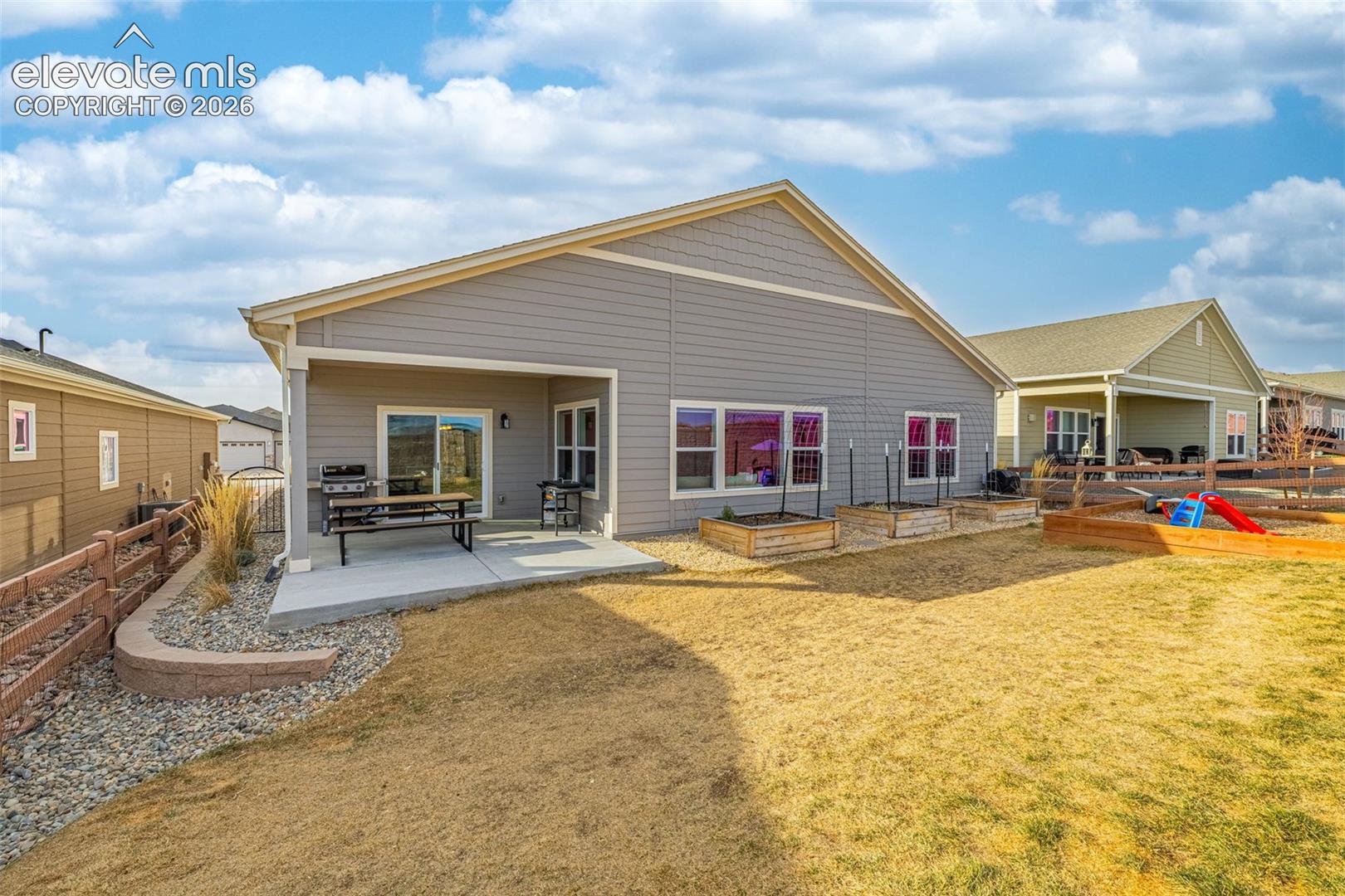 Home’s rear exterior with a covered patio, outdoor dining set, grill, and raised garden beds.