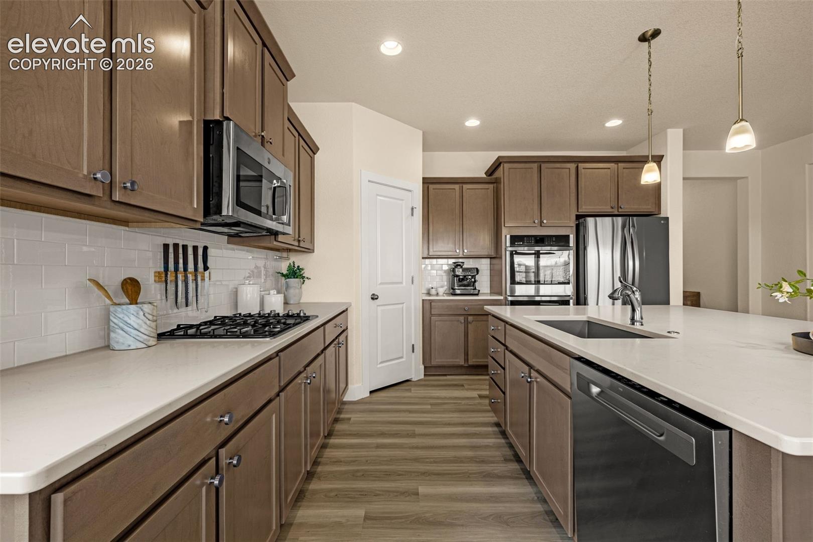 Kitchen with brown cabinetry, white counters, gas cooktop, stainless appliances, and a large island.