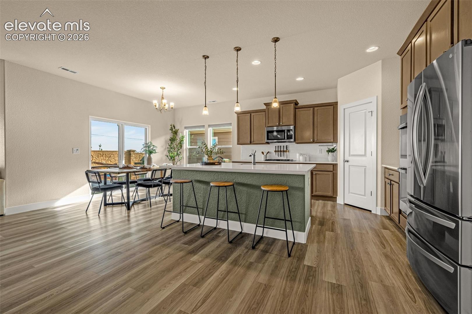 Kitchen with green island and bar stools, brown cabinets, stainless appliances, and a dining area by sliding glass doors.